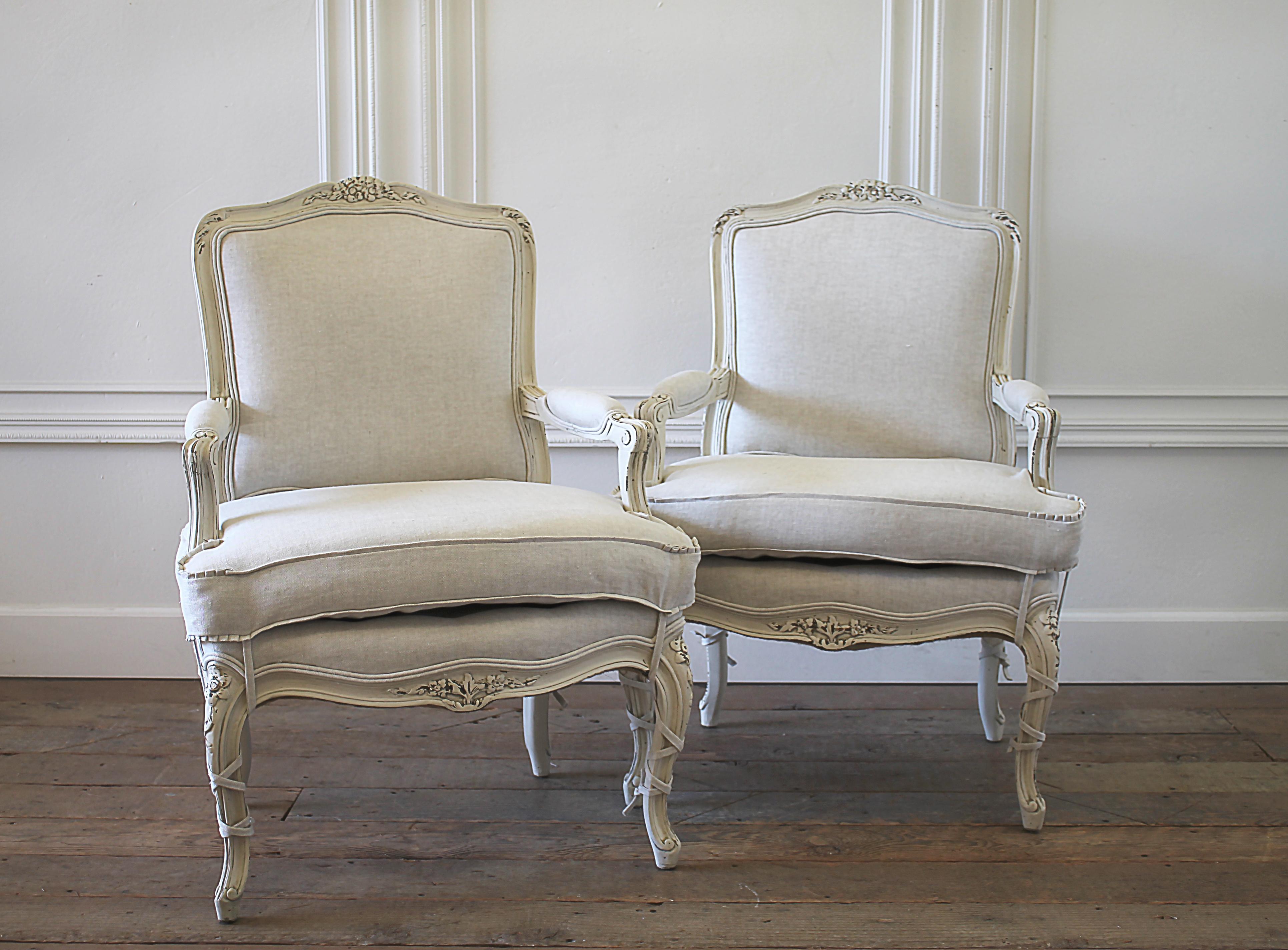 Pair of painted and upholstered Louis XVI style bergère chairs in natural linen. Painted in our soft oyster white, with subtle distressed edges, and finished with an antique glazed patina. This off white color blends beautifully with all shades of