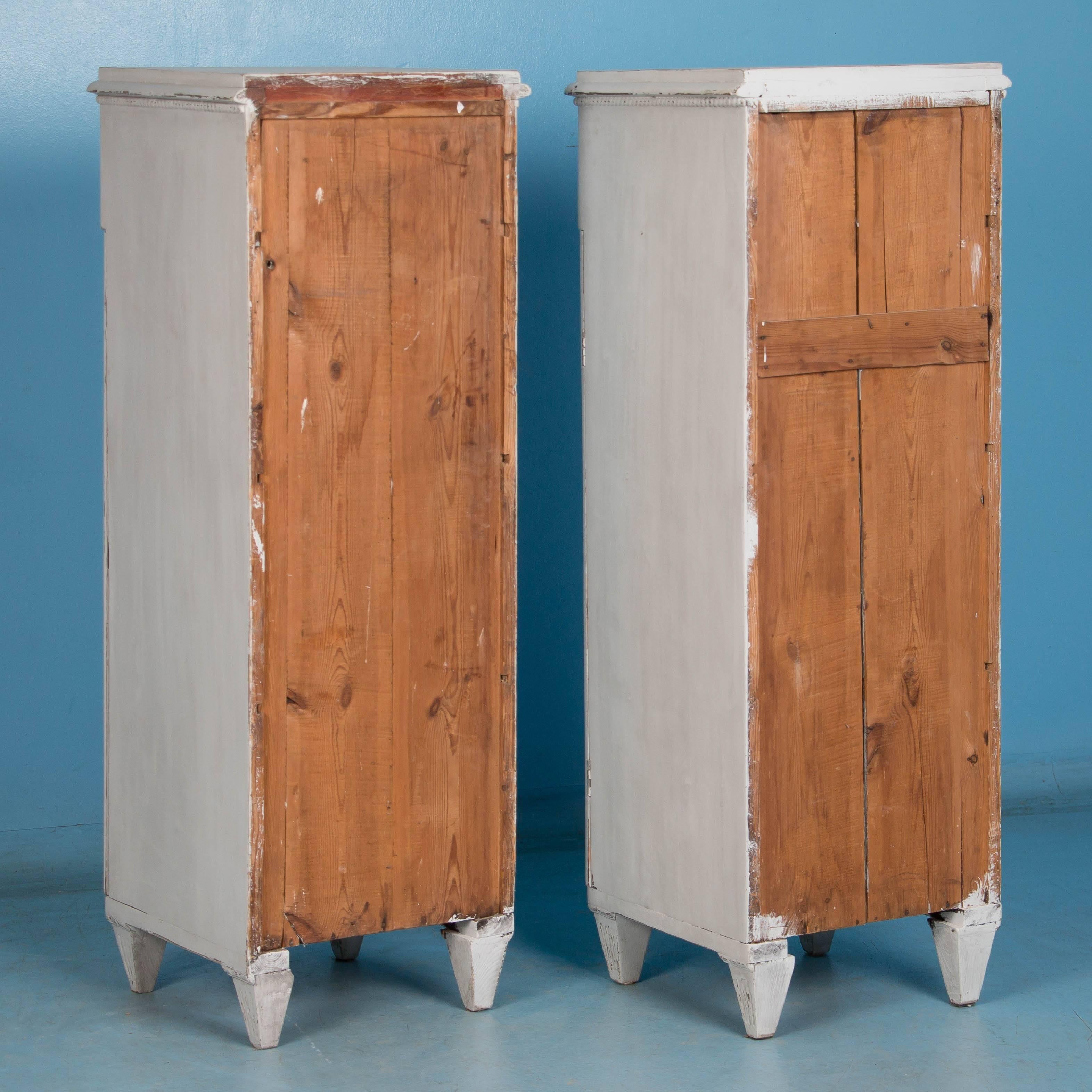 This unique pair of narrow matching cabinets are from the late 1800s and were handcrafted in Sweden. The distressed soft white paint was recently added, fitting the Gustavian style and enhancing the carved fluted panels of both cabinets. The single