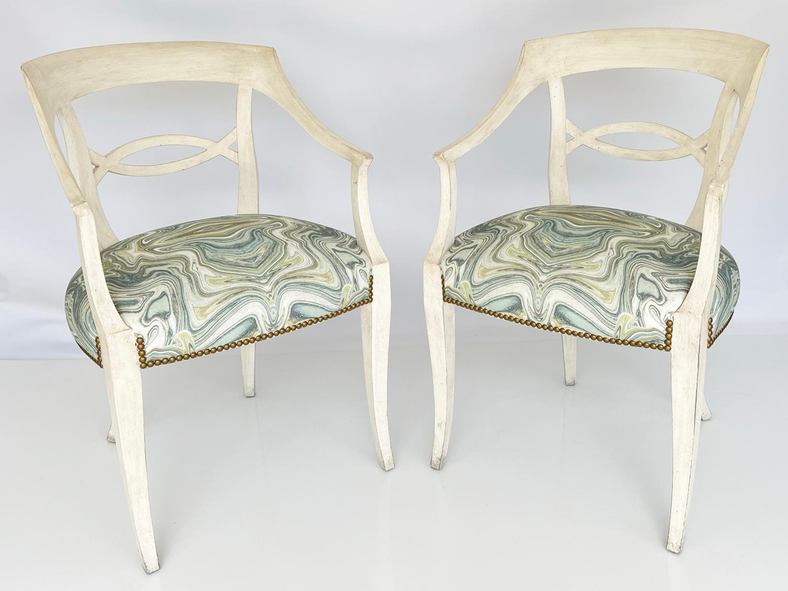 Pair of armchairs, by Baker, each having an ivory painted finish showing natural wear, its bowed backrest extending to outswept arms, flanking the arched and crossed backsplat, over a crown seat, upholstered with nailheads, and raised on