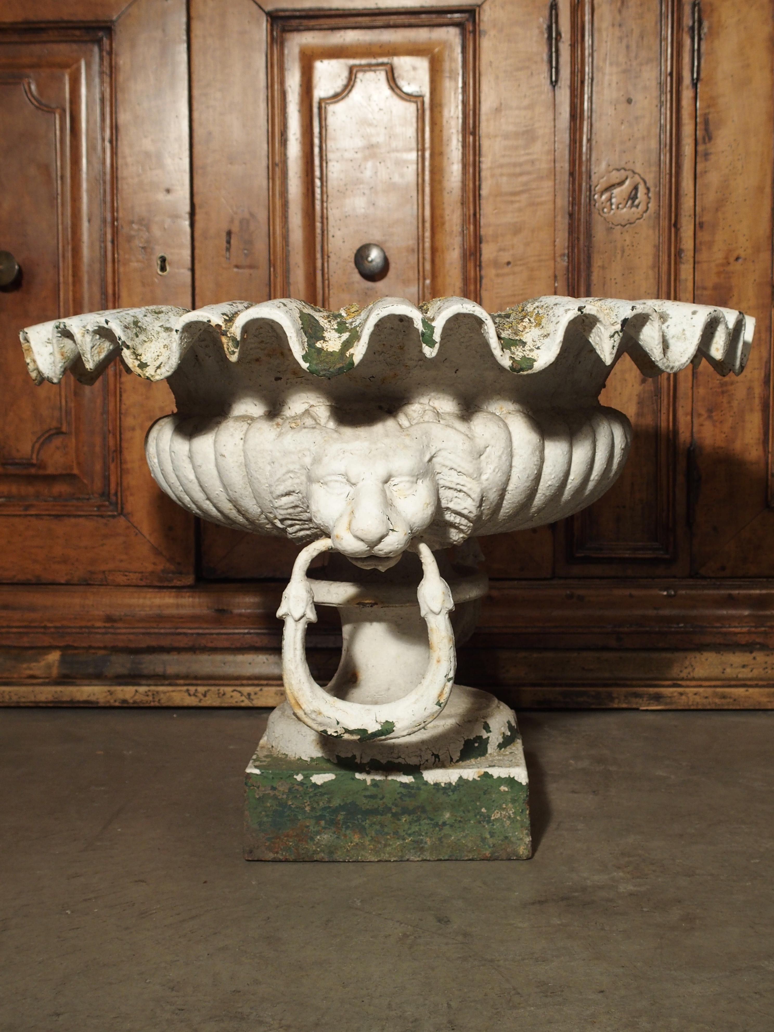 From France, these graceful, painted, cast iron urns have fabulous lions mask handles with rings in their mouths. At the top are linear ruffles going around the periphery of each urn. Below this are gadrooned lobes and an indention at the waist