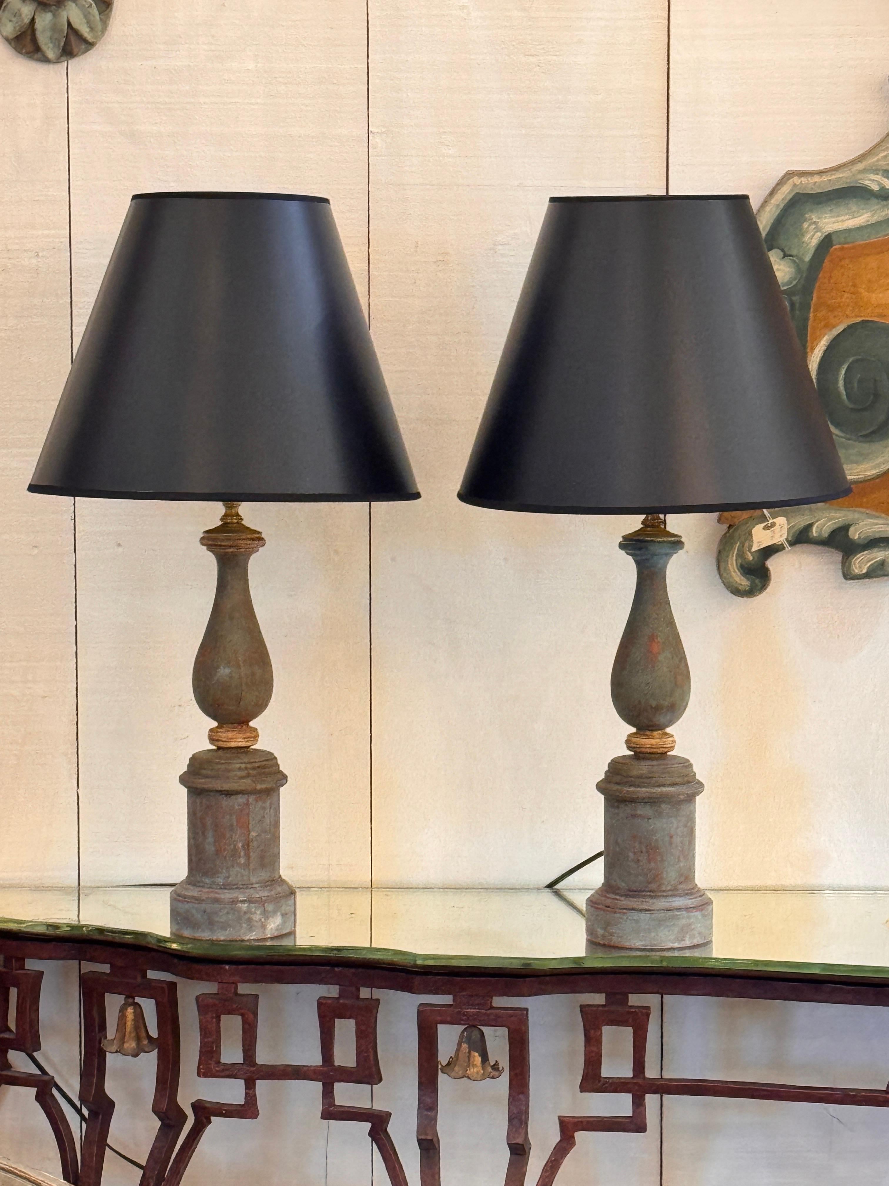 Coppia di lampade da tavolo dipinte con forme a balaustro tornite su basi a colonna cilindriche. La superficie invecchiata dalle intemperie mostra un pigmento stratificato di colore grigio-blu tenue con sfumature rosse calde, che conferisce alla