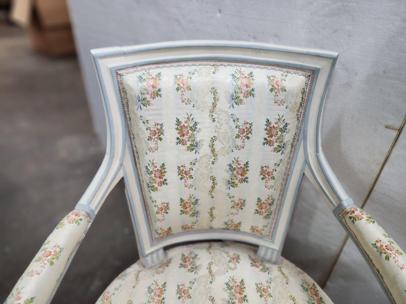 These French Directoire style open arm chairs from around 1910 are a charming and elegant pair. With gently curved arms and delicate carved details, these chairs exude a timeless appeal. They are painted in a soft, neutral color and feature plush