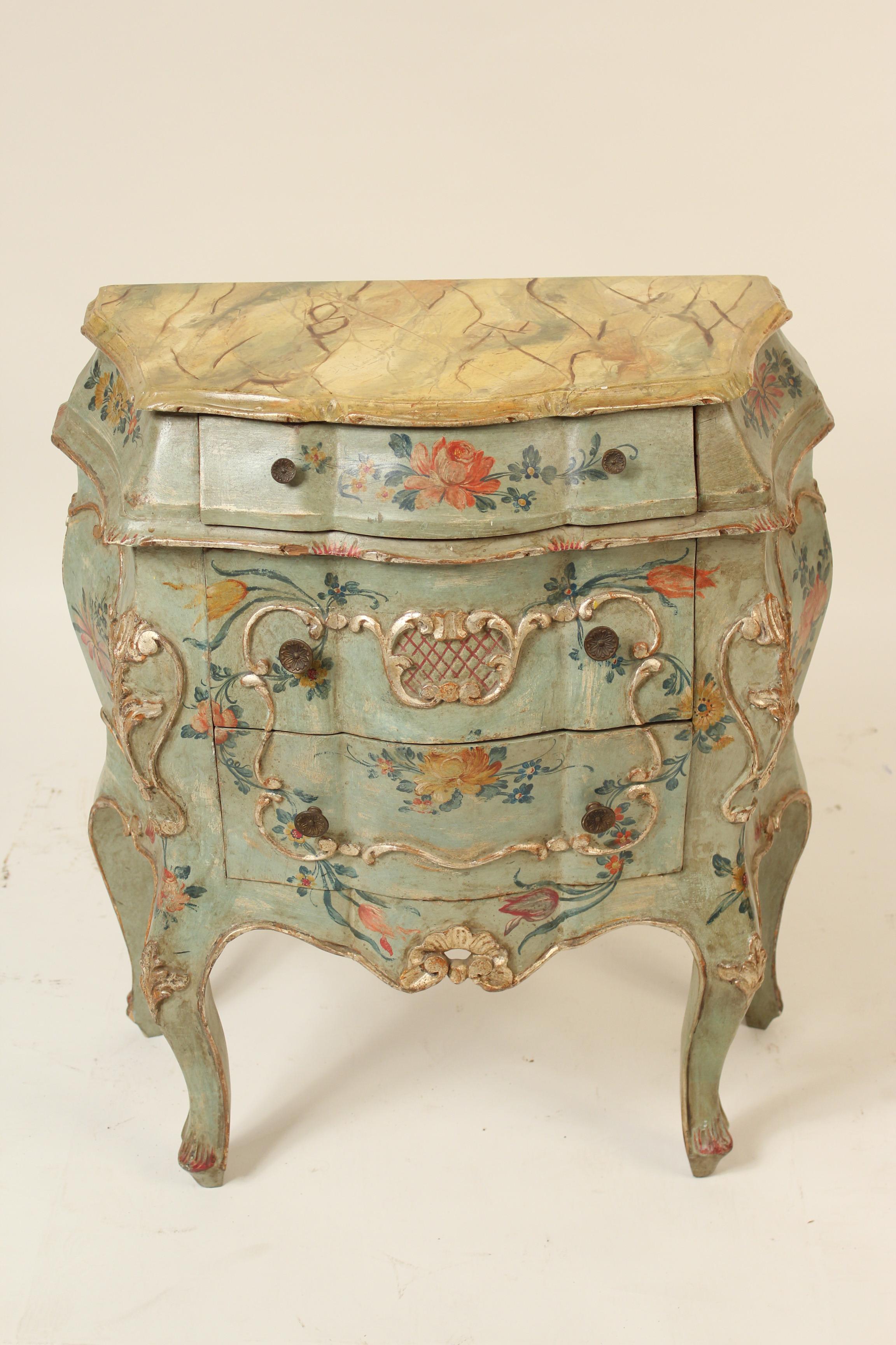 Pair of Italian Louis XV style painted and silver leaf bombe commodes with faux marble tops, circa 1960s.