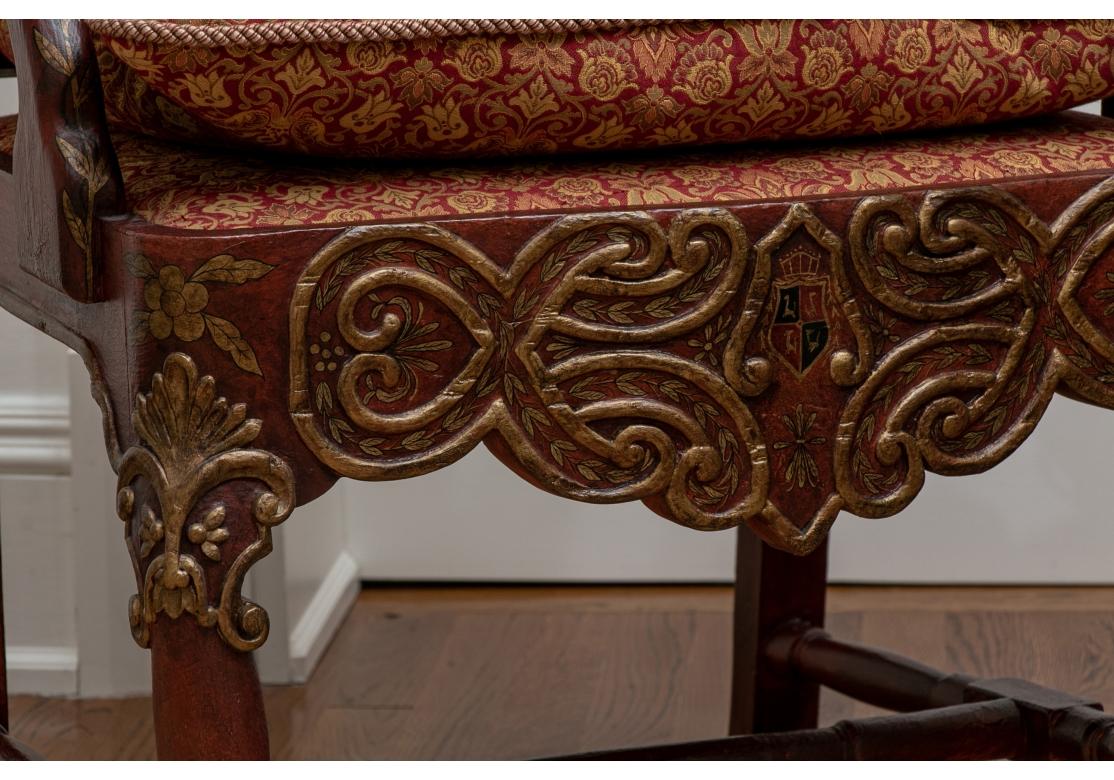 Carved in a burgundy and gilt finish with elaborate scrolled backs and lion mask crests. Gilt floral details, curved arms , and elaborate scroll decorated seat rails with crests. The front legs with ball-and-claw feet, back splayed legs, and H