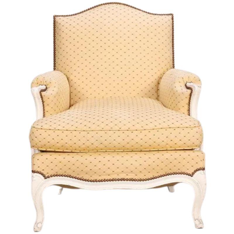 A vintage pair of Louis XV style bergere chairs with a painted antique white arched frame, upholstered seat, back and arms and painted curved legs, a diamond print yellow fabric, and nail head trim to front and back.