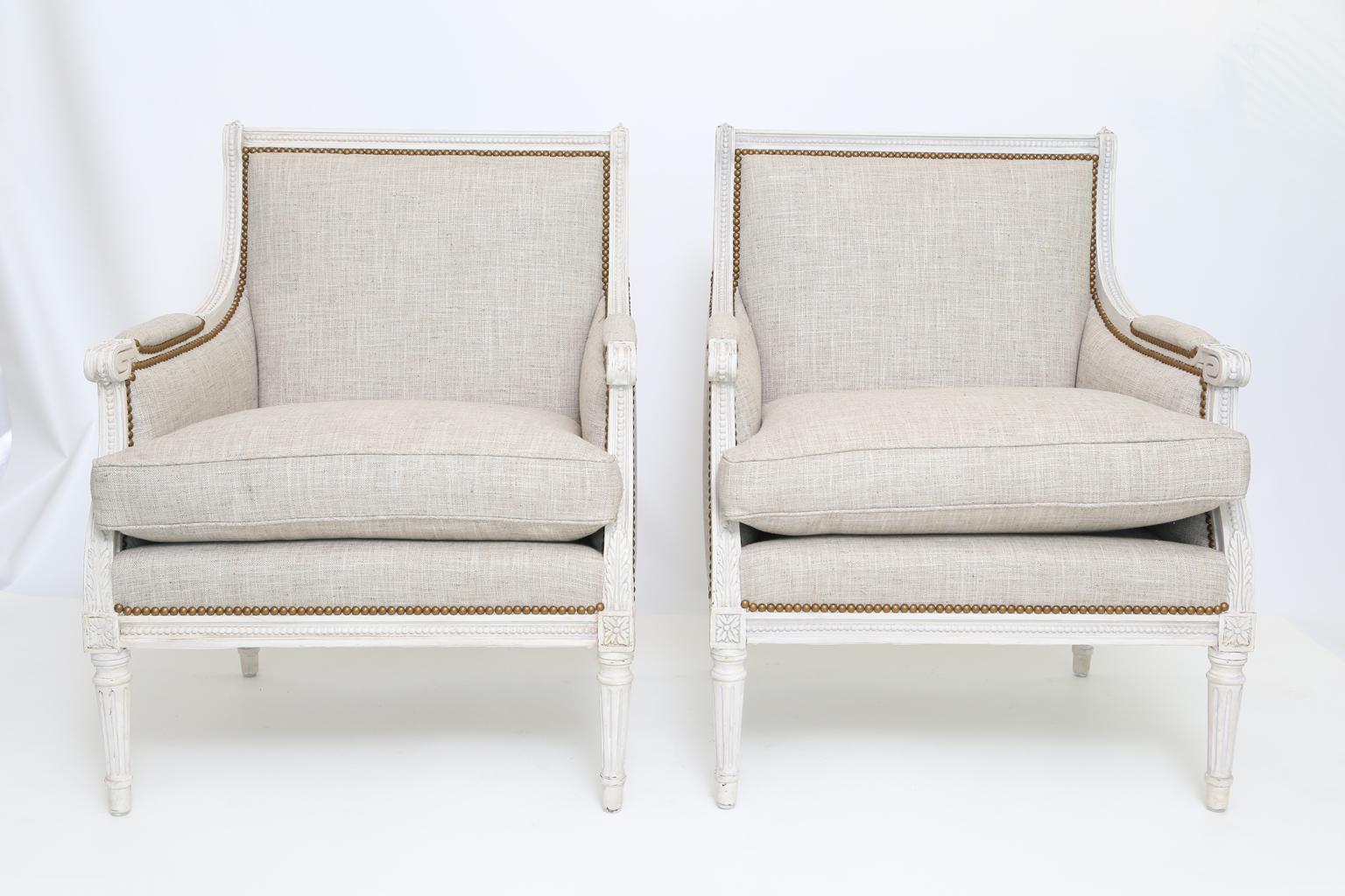 Pair of upholstered closed armchairs, in Louis XVI taste, each having a painted frame showing desirable wear, channeled frames inset with beading, the straight toprail flanked by finials, the padded armrests ending in scrolls, on downswept