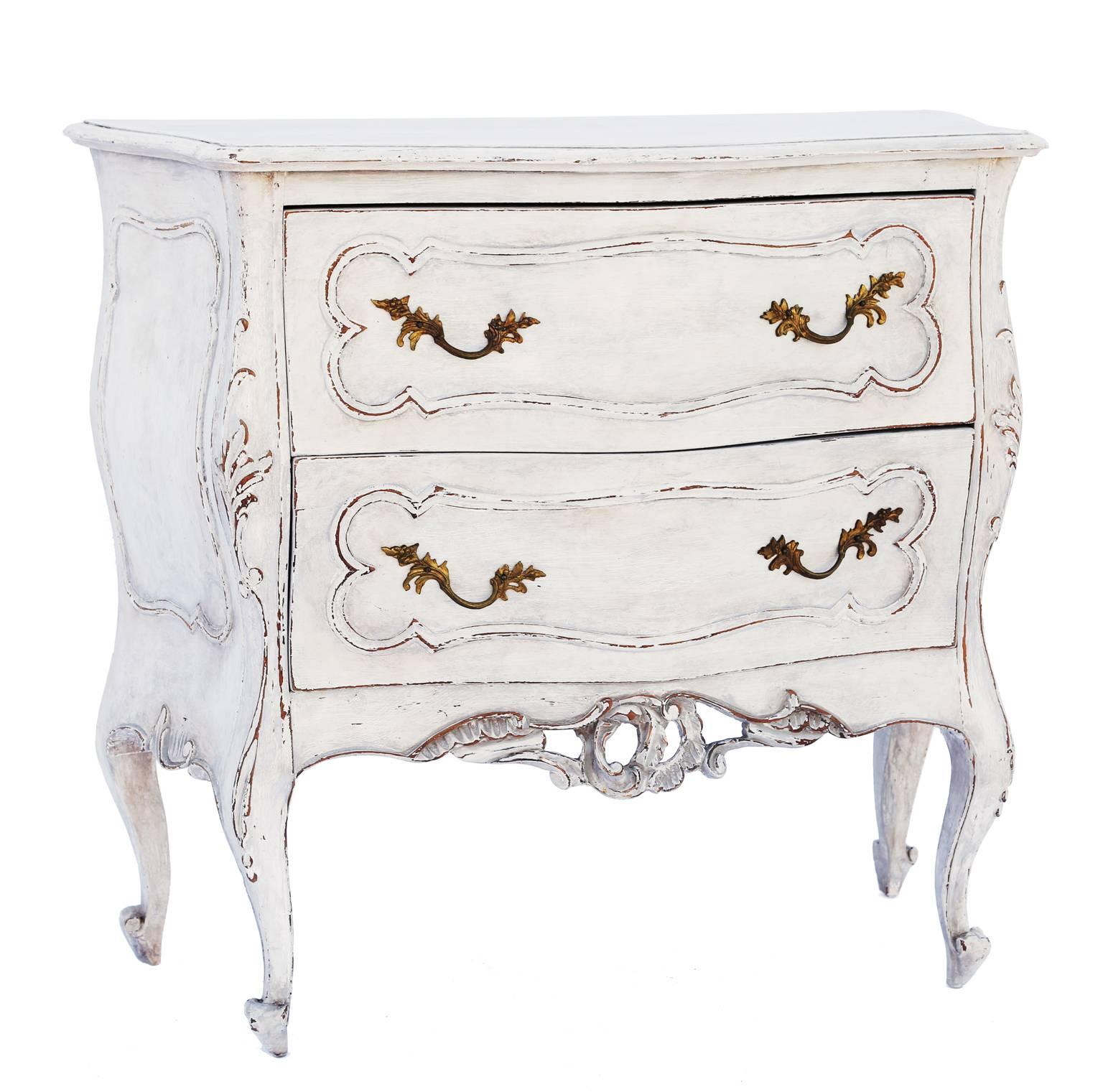 Pair of commodes, in the Rococo style, each with a painted finish showing natural wear, free-form molded top on raised and fielded, double stacked drawers, with brass rocaille handles, bowed sides with its stiles outcarved with foliate vines, raised