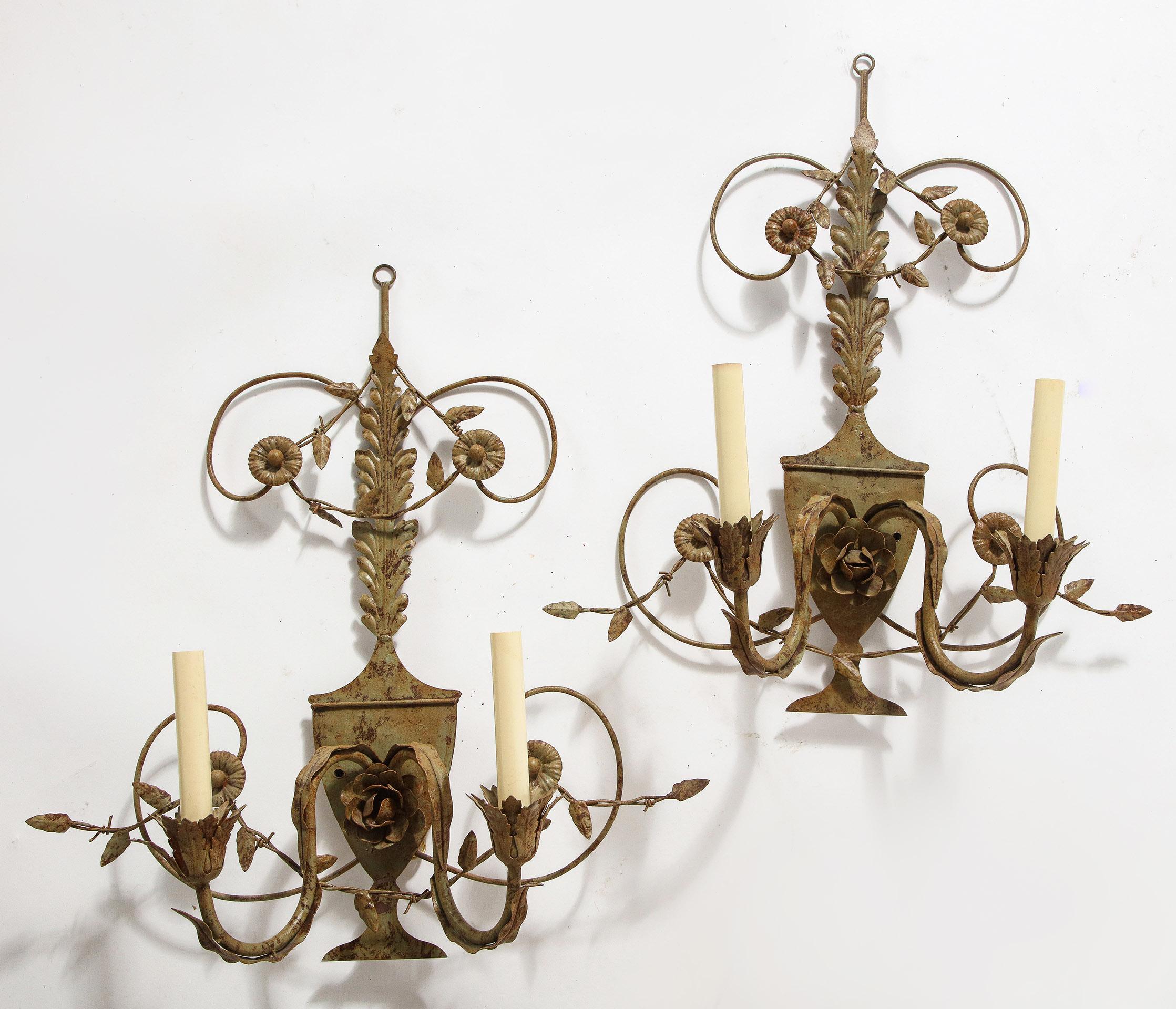 The pair of painted tole 2-light sconces, having an urn form back plate with a stylized floral design above, the back plate supporting 2 floral and leaf decorated candle arms.

electrified.