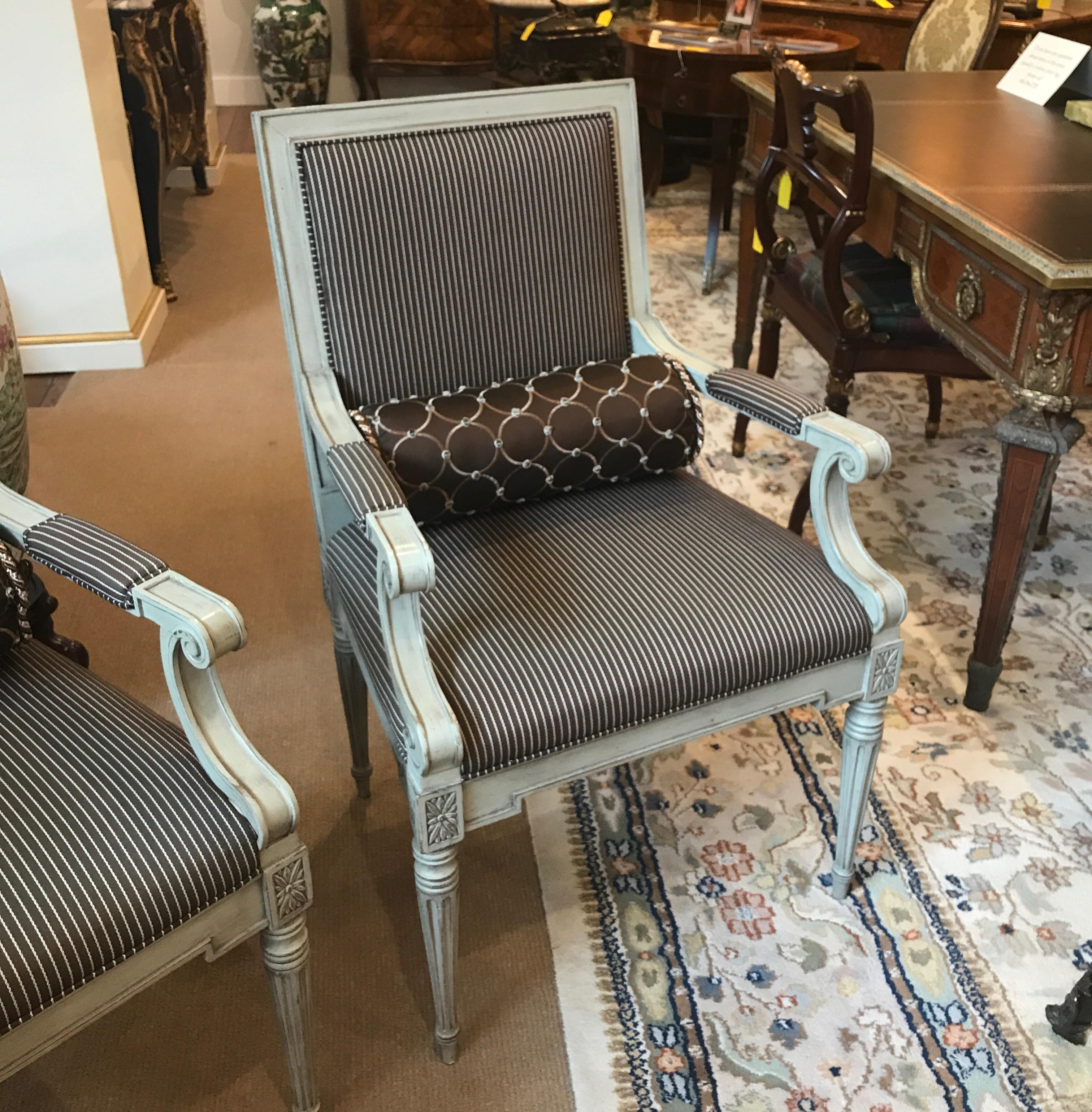 Sophisticated pair of painted walnut framed Louis XVI style armchairs is woven stripped chocolate and cream fabric. The light putty gray frames with carved details and tapering reeded legs. The chairs each come with a round silk lumbar pillow.