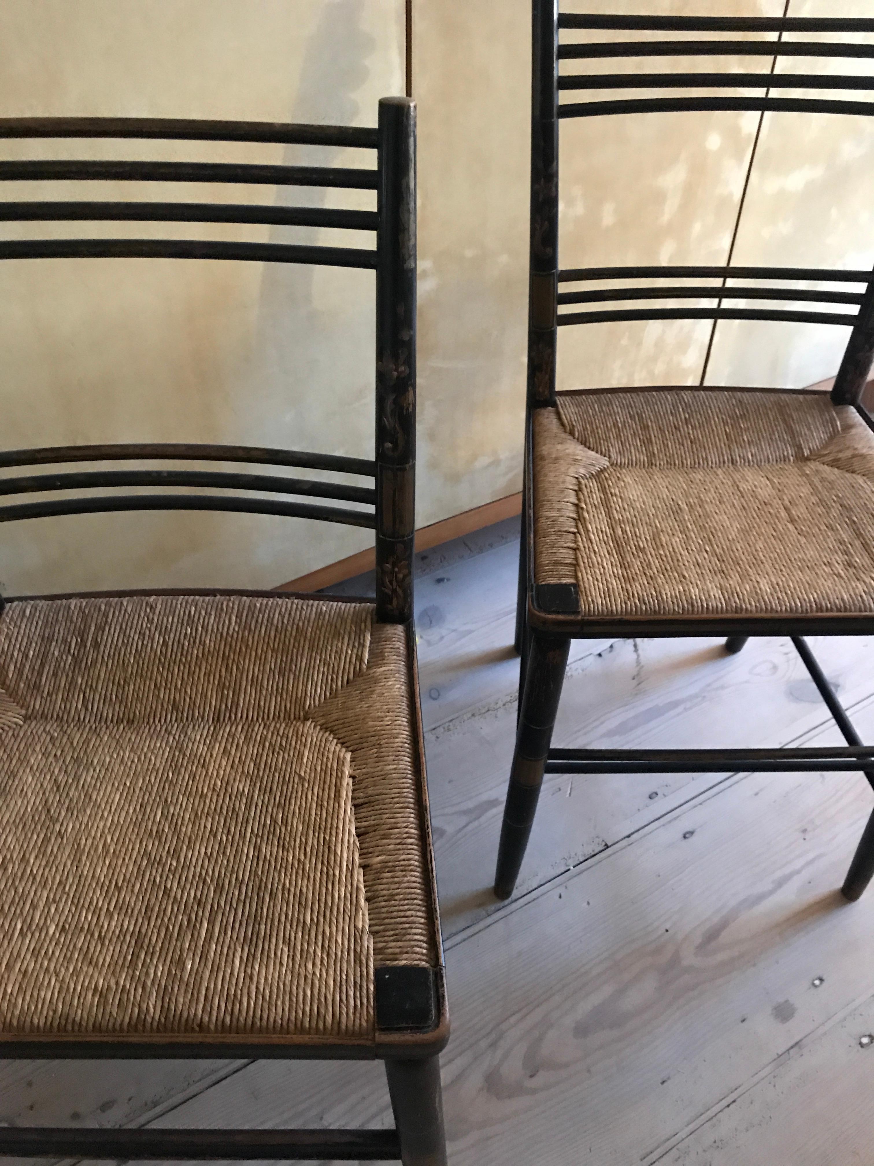 An elegant pair of black painted wooden chairs with golden floral decorations. Woven seaweed seats.