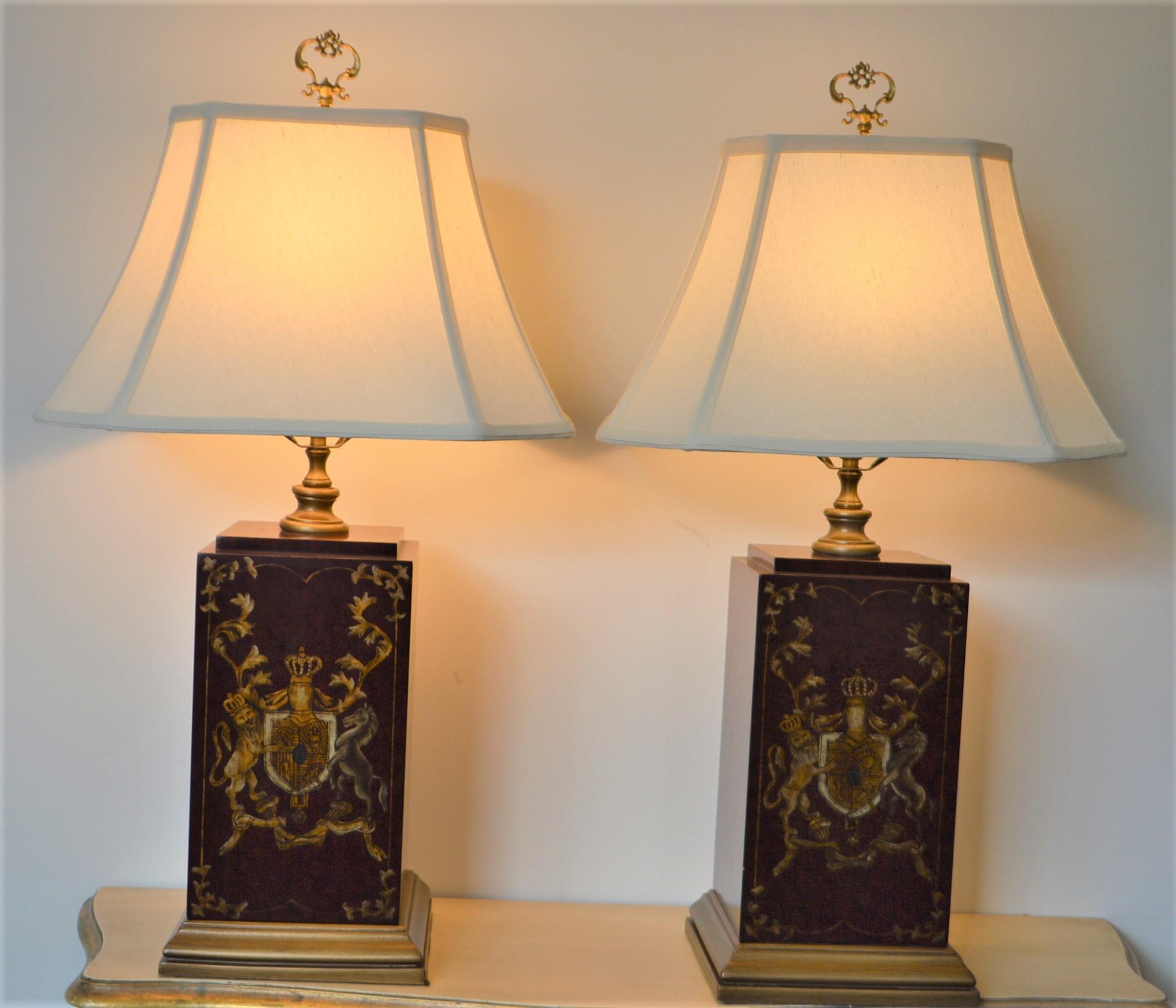 Unusual square base wooden lamps that have been decoratively painted with armorial design on two sides and lute and ribbons on the other two sides. The color is manly burgundy red with the gold accents in the painted area.
The shades are cream and