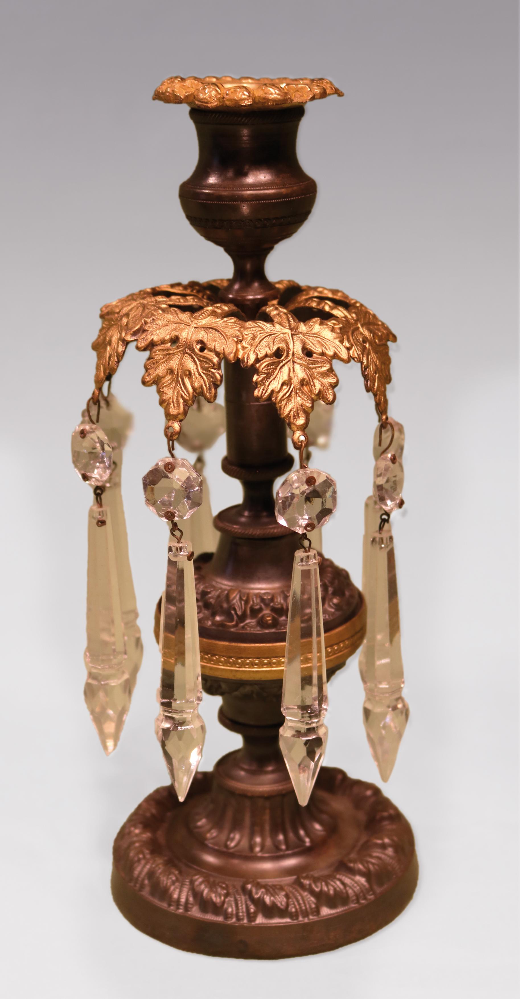 A pair of early 19th century Regency period bronze and ormolu lustre candlesticks having floral sconces above leaf canopies and bulbous stems with engine-turned central ring, raised on circular bases.