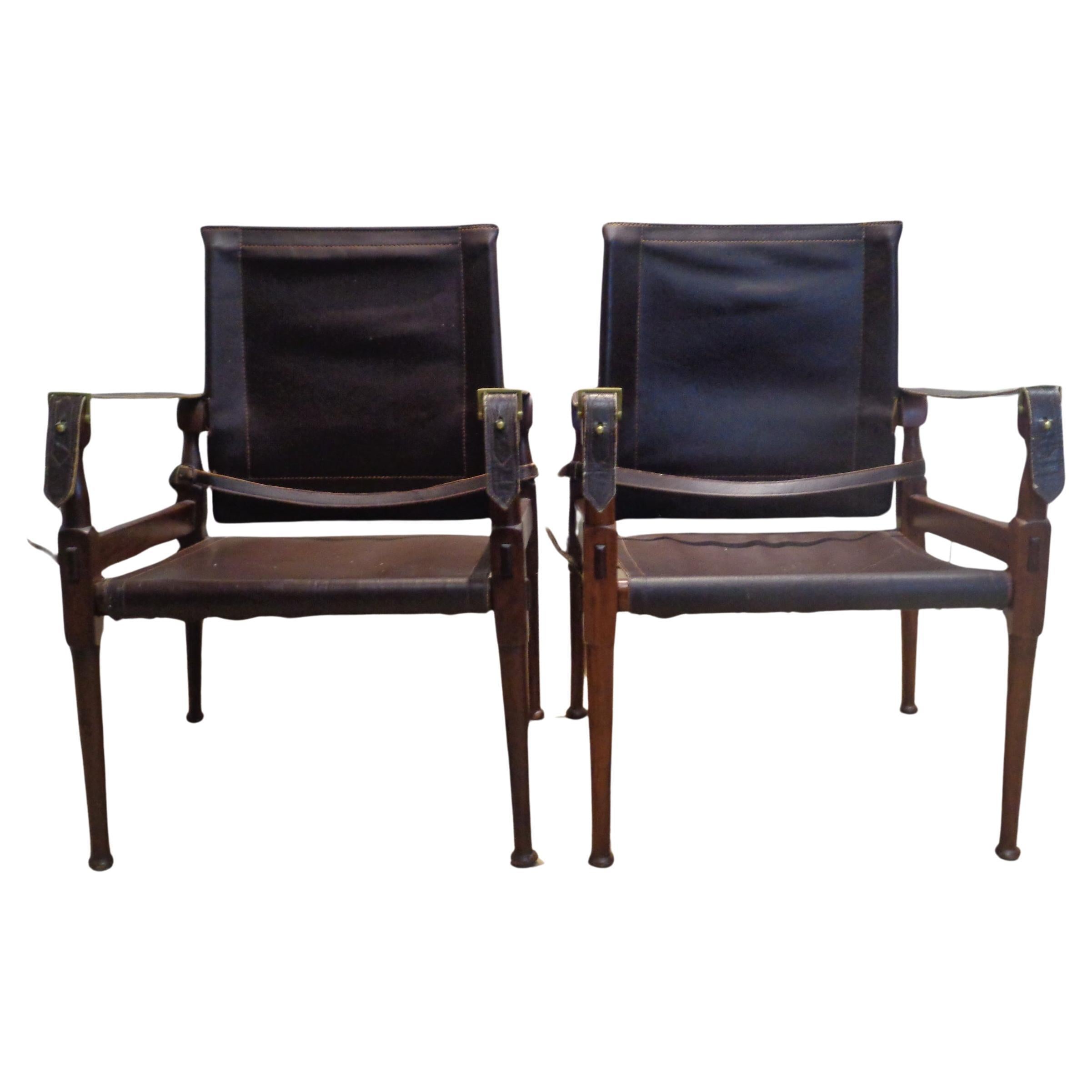 Pair of safari chairs in the British Colonial Campaign style. Mahogany framework  w/ turned and mortised construction and beautifully aged color / dark chocolate brown stitched leather seats and backs / stitched leather arm straps w/ brass buckles,