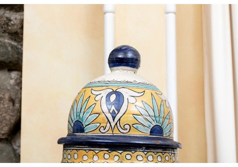 Very large lidded jars with shaped bulbous forms tapering to the bases. Decorated in yellow and blue on white with medallions with floral baskets on the shoulders. Yellow floral bands separate the lower geometric motifs. The lids with complimentary
