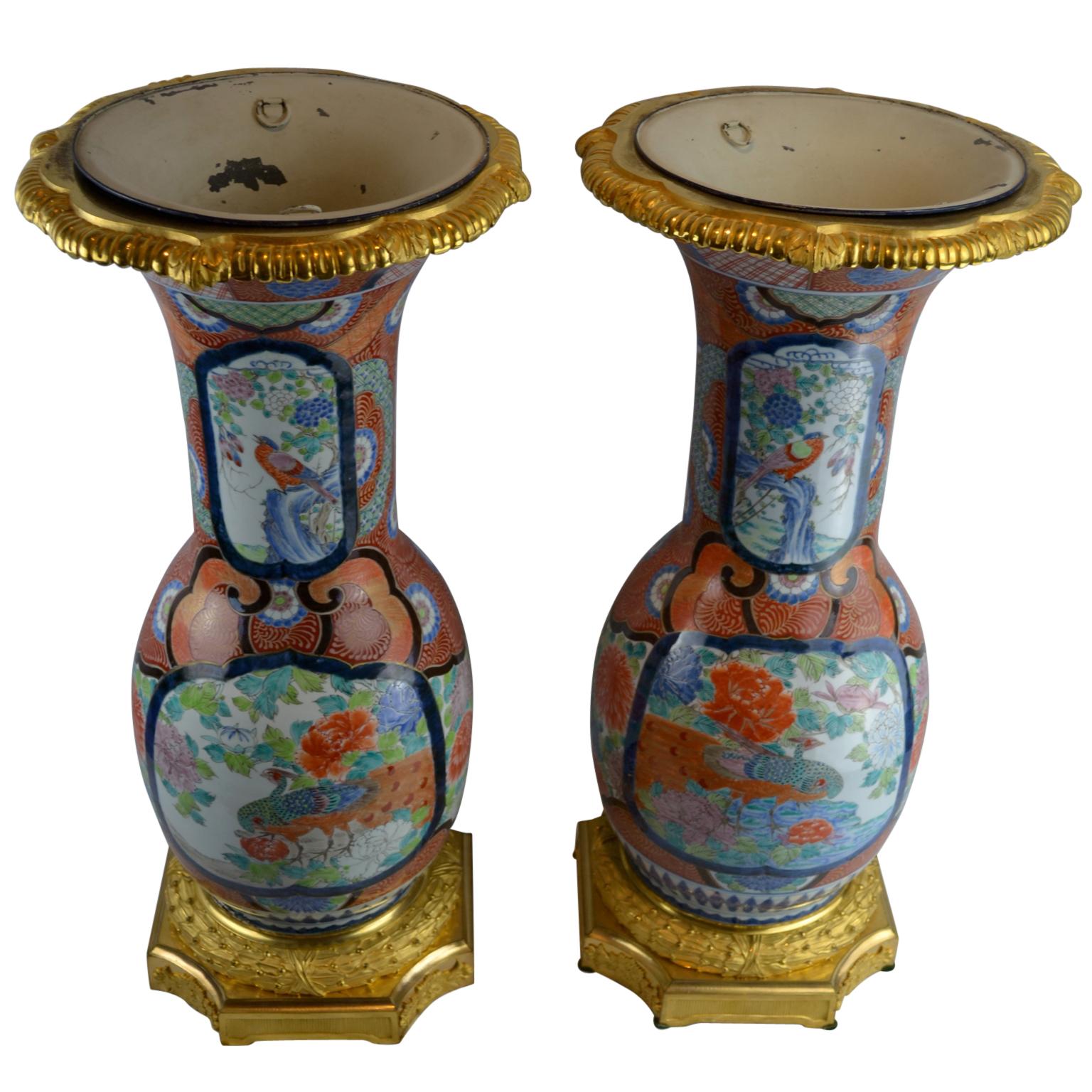 An impressive pair of late 19th century Japanese Imari porcelain vases decorated with colourful peacocks, other birds, flowers, chrysanthemums, manufactured for export to France where the finely chased gilt bronze bases and rims were added. The