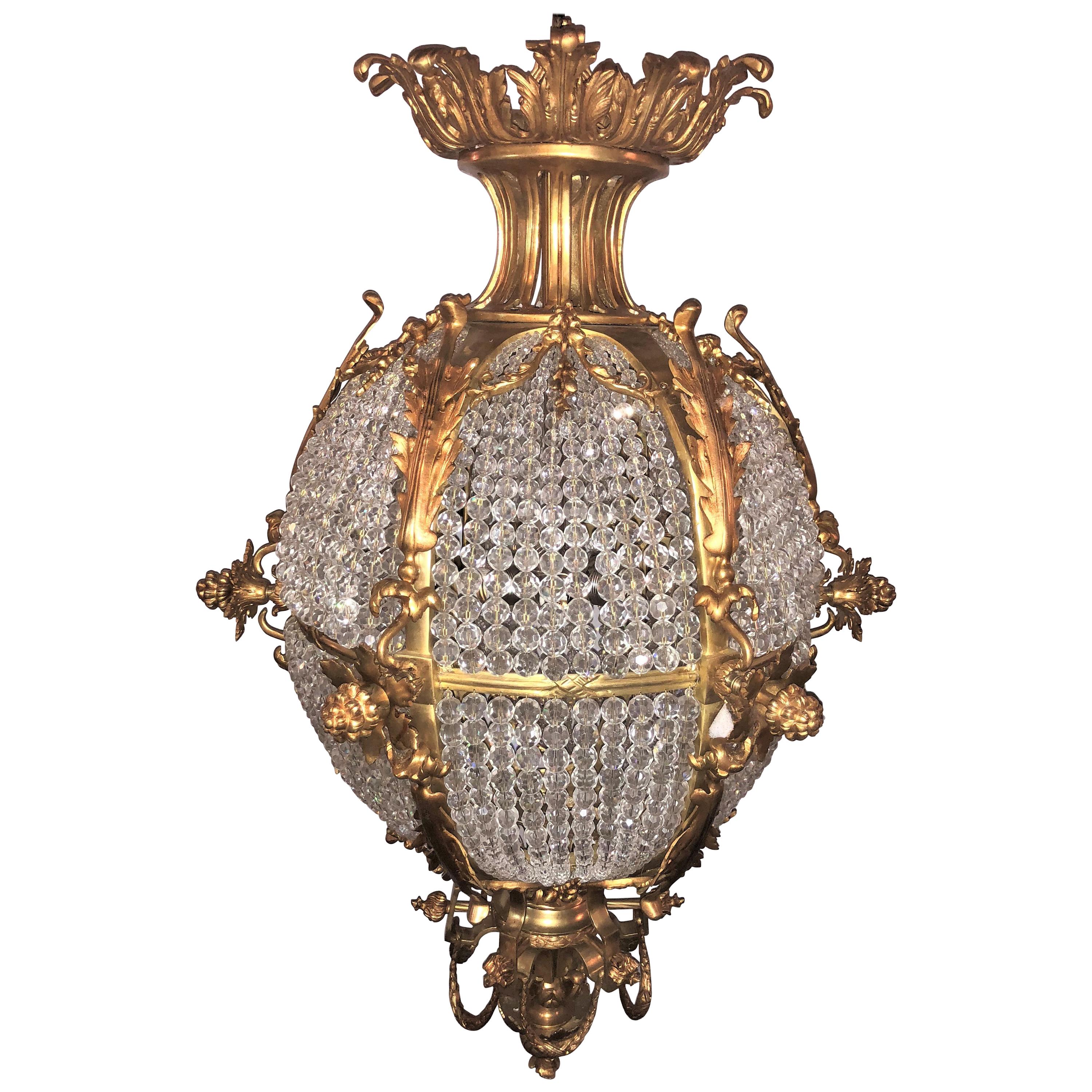 A pair of doré bronze circular crystal beaded ball chandeliers. Each of these palatial round chandelier take five bulbs and have been totally rewired. The spectacular bronze work framing a large crystal beaded sphere with a door opening to clean and