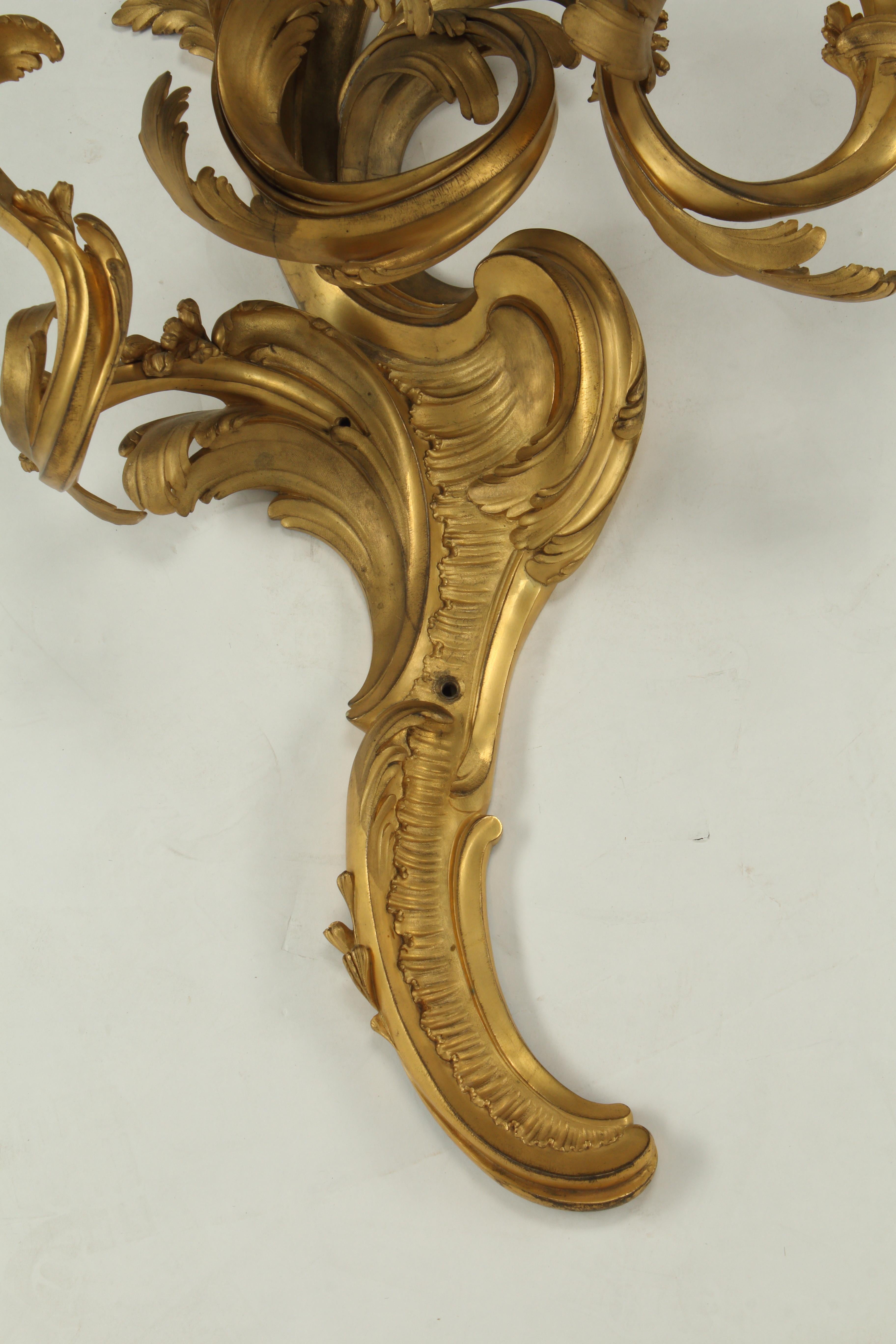 Questa coppia di appliques in bronzo ormolinato in stile Luigi XV presenta le caratteristiche linee asimmetriche e fluide dell'epoca. Ogni applique ha tre rami che curvano intricatamente verso l'alto e sostengono delicati portacandele con motivi