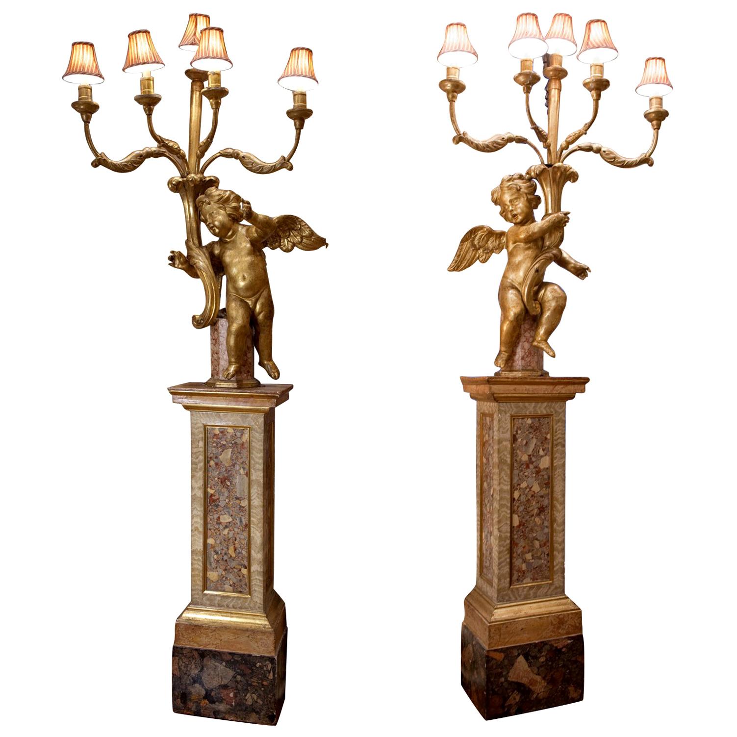 This pair of magnificent torcheres are of the finest quality carved wood, gilding and faux marble painting.  Each are comprised of a giltwood cherub or putto figure sitting on faux marble double bases holding aloft five scrolling giltwood candle