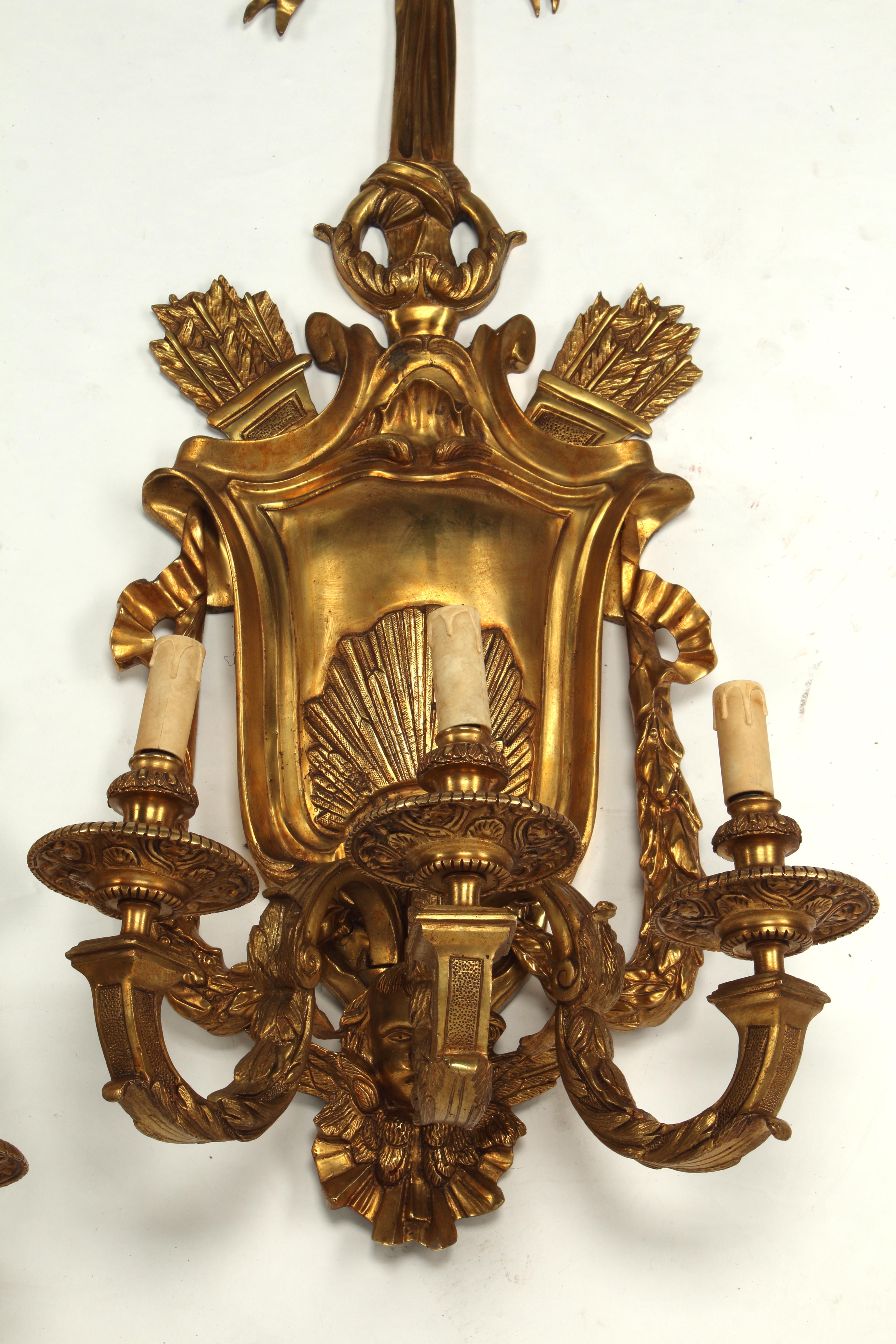 Cette paire de scones muraux de style Louis XV illustre l'esthétique opulente de la période Louis XV. Chaque applique comporte un écusson central avec des moulages de coquillages et est surmontée d'un grand nœud orné d'un ruban qui se déploie de