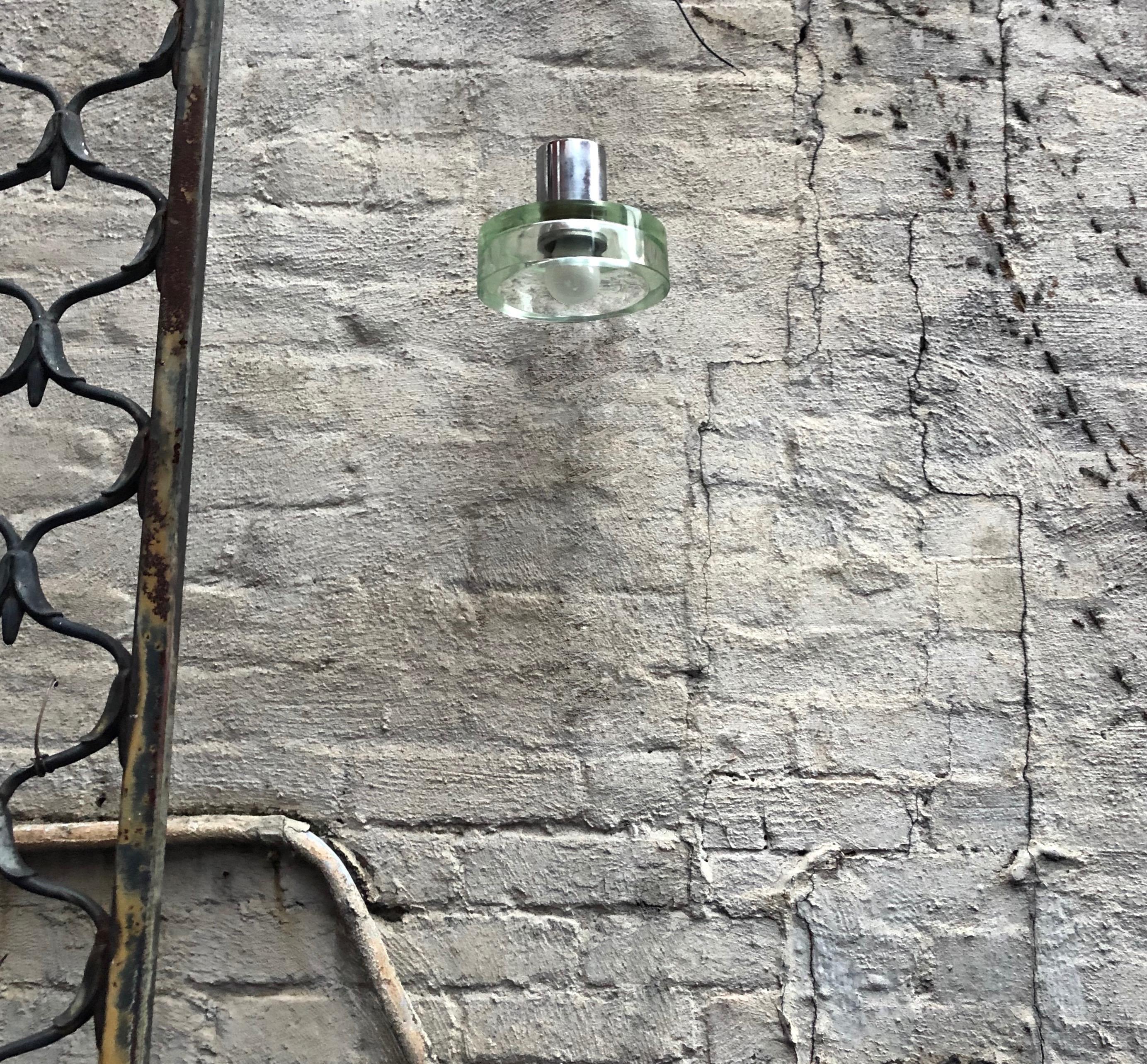 Pair of sconces designed by Flavio Poli for Seguso each with nickel plated hardware and a rectangular mounting plate, all that support a round, pale green, 1.8 cm thick glass diffuser. Each sconce has a single US standard socket, and the lights can