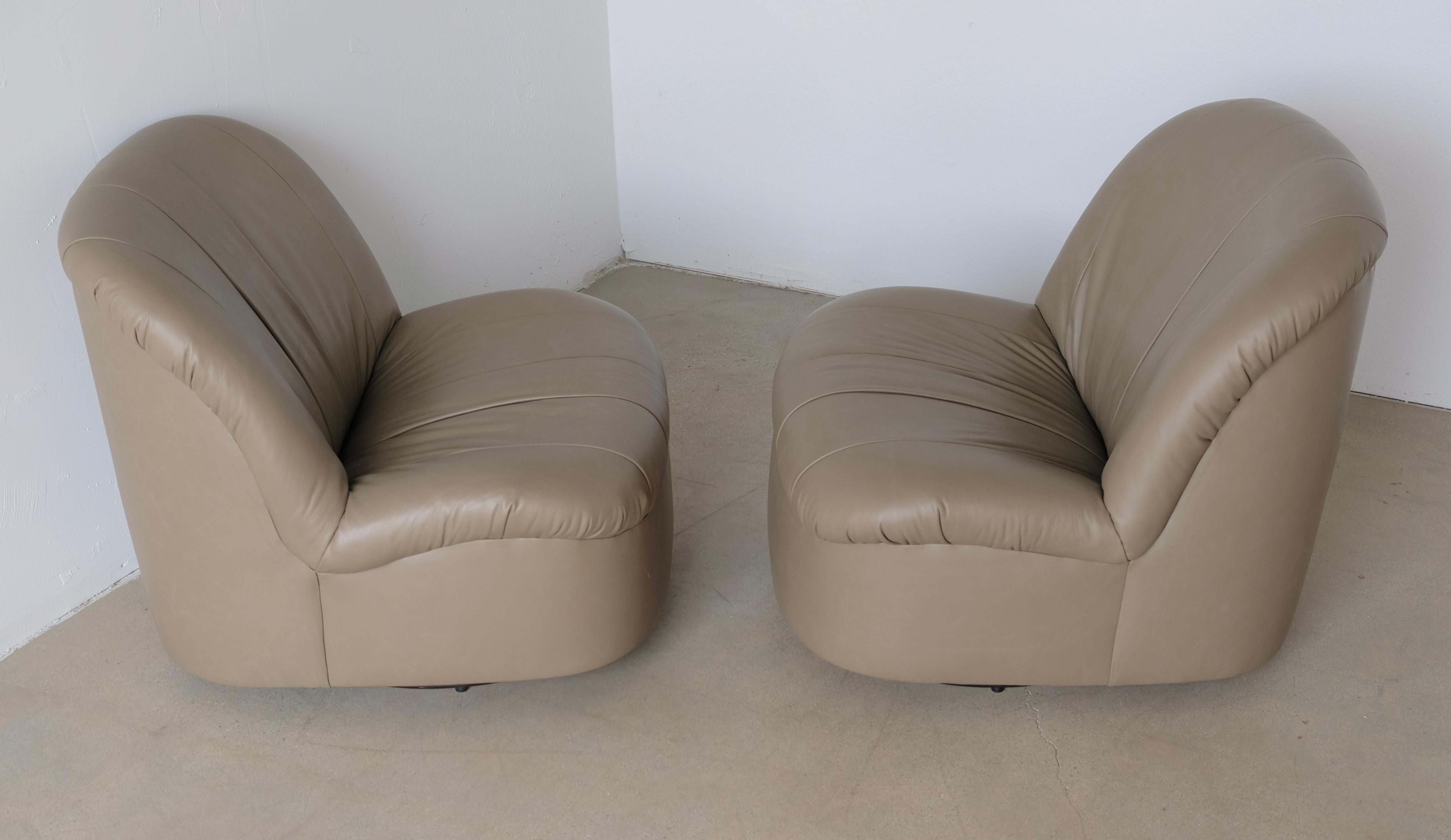 These Postmodern Italian style low slung pair of slipper lounge chairs tilt and swivel. They have been recovered in a pale sage green olive leather. They sit very comfortably.