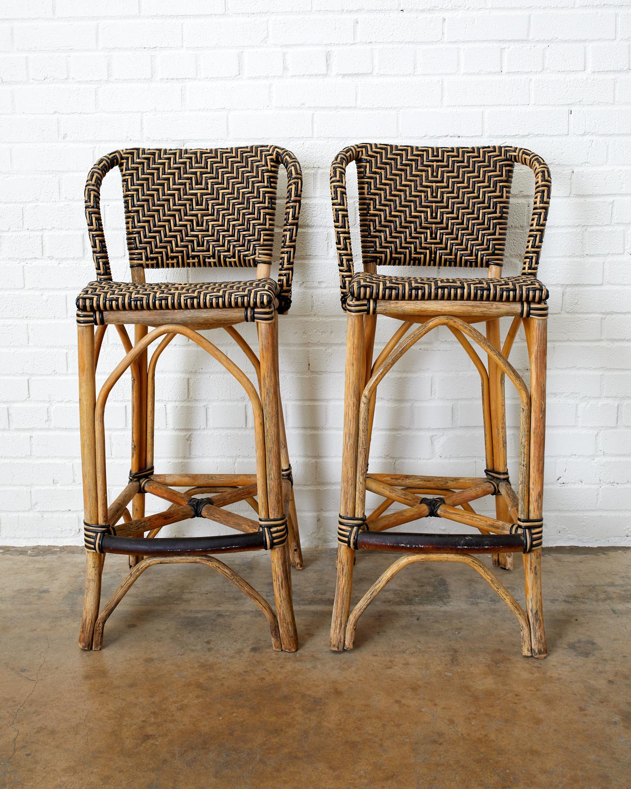 Handsome pair of bistro style patio garden bar stools. Constructed from bamboo rattan poles featuring a woven chevron pattern design made of wicker and synthetic rattan. Made by Palecek in the organic modern style after French Art Deco inspired