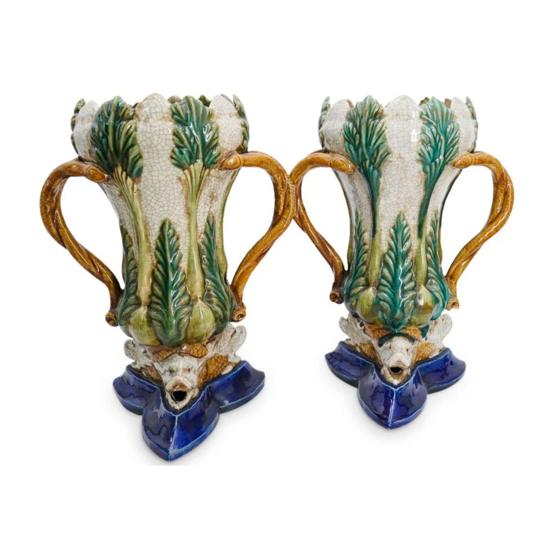 Questa coppia di vasi in maiolica smaltata presenta un intricato motivo di palme con un sorprendente fogliame verde su uno smalto crepla strutturato. Ogni vaso è ornato da basi a forma di delfino in una ricca tonalità di blu, che mette in mostra