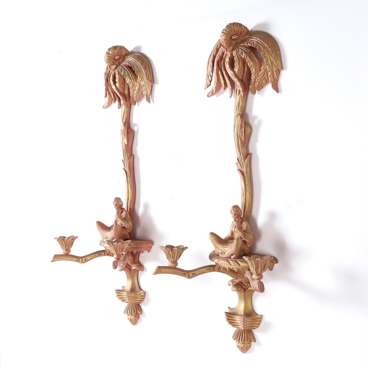 Pair of two light Italian carved wood wall sconces having palm trees over a platform with a seated chinoiserie figure, faux bamboo arms supporting floral candle cups, and a red and gold finish.