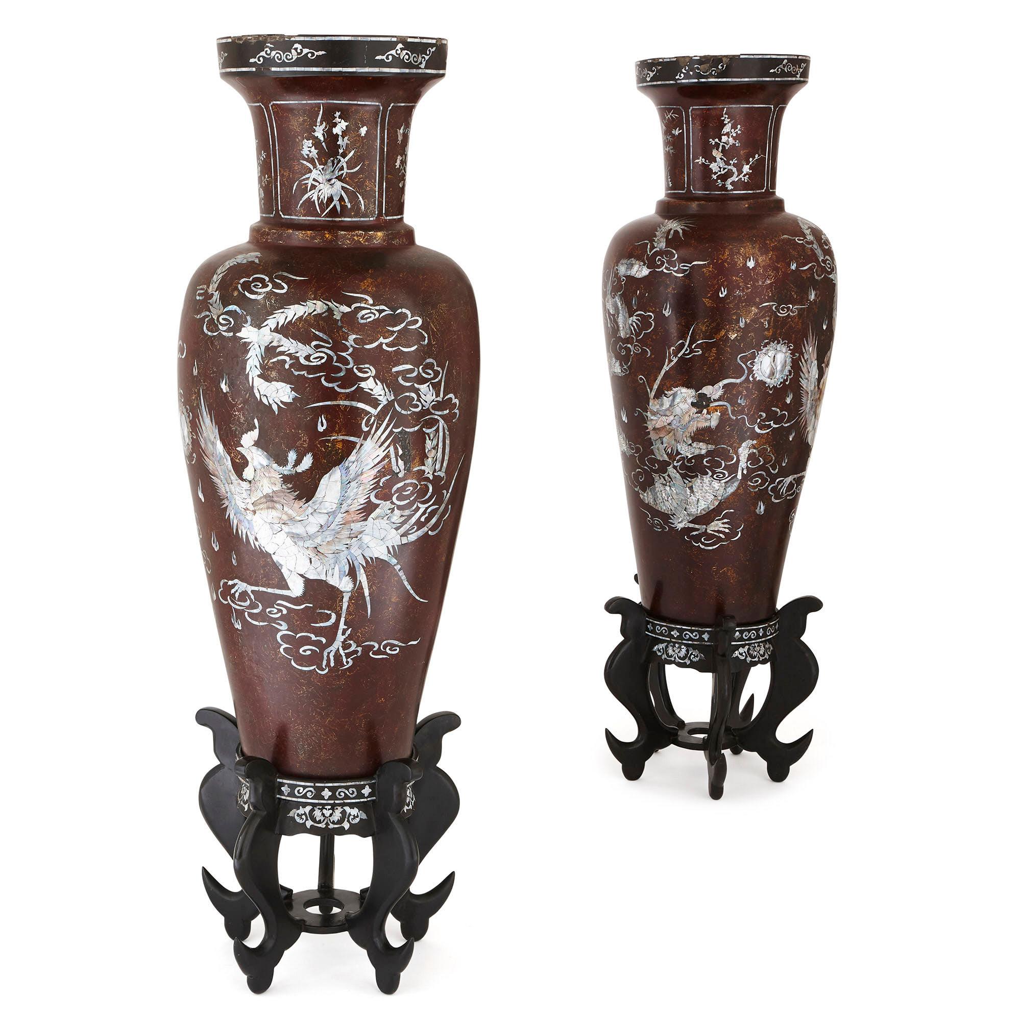 Dieses Paar großer chinesischer Pappmaché-Vasen hat einen braunen Grund und umfangreiche Perlmutt-Intarsien. Die Intarsien sind so angeordnet, dass auf jeder Vase die Darstellung eines fliegenden Vogels inmitten von Wind und Laub zu sehen ist. Jede
