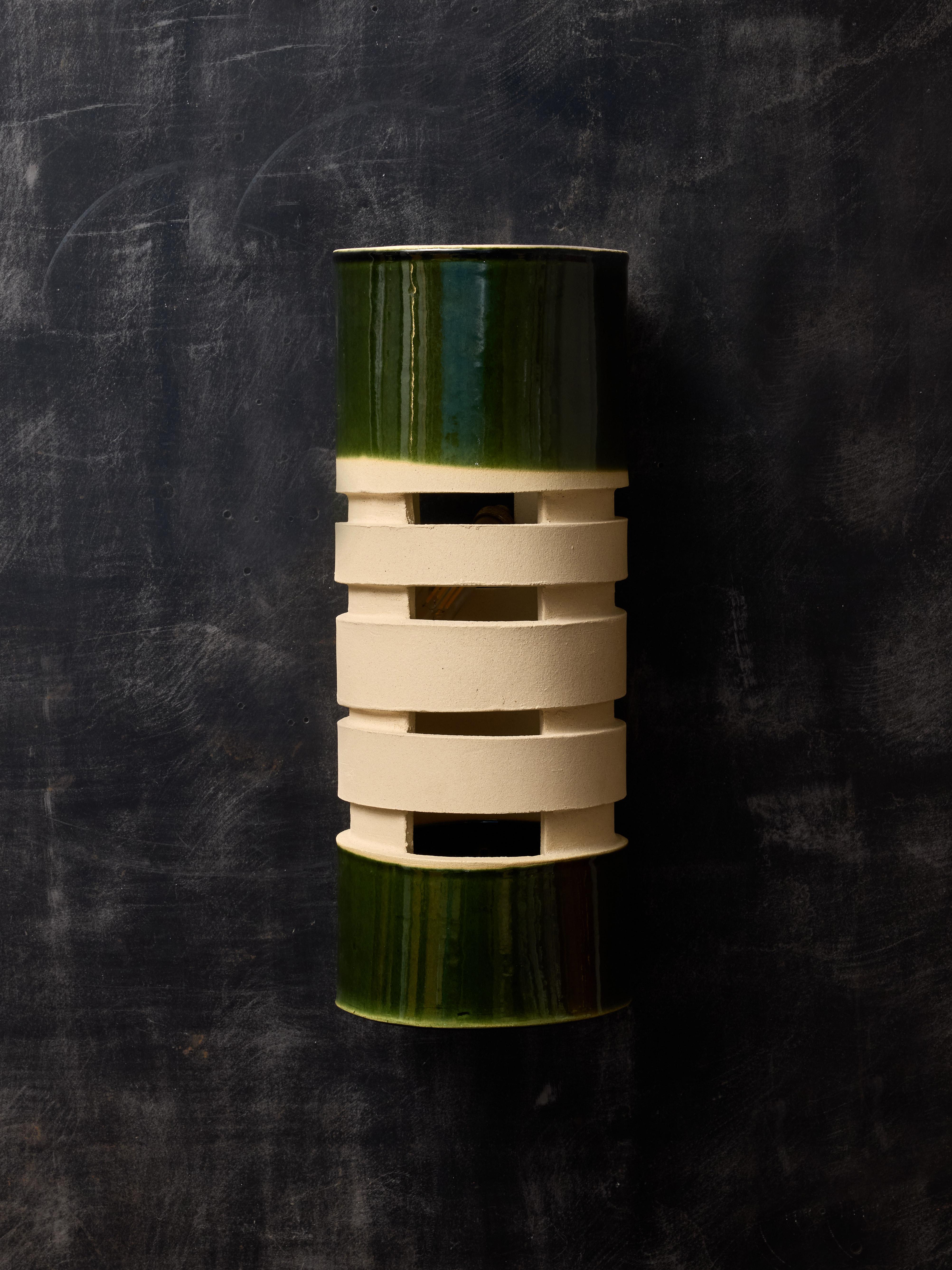 Un par de apliques de pared diseñados por Amandine Gorrino, elaborados a partir de una única pieza de cerámica tubular. Presentan un rico vidriado verde tanto en la parte superior como en la inferior, adornado con una serie de aberturas decorativas