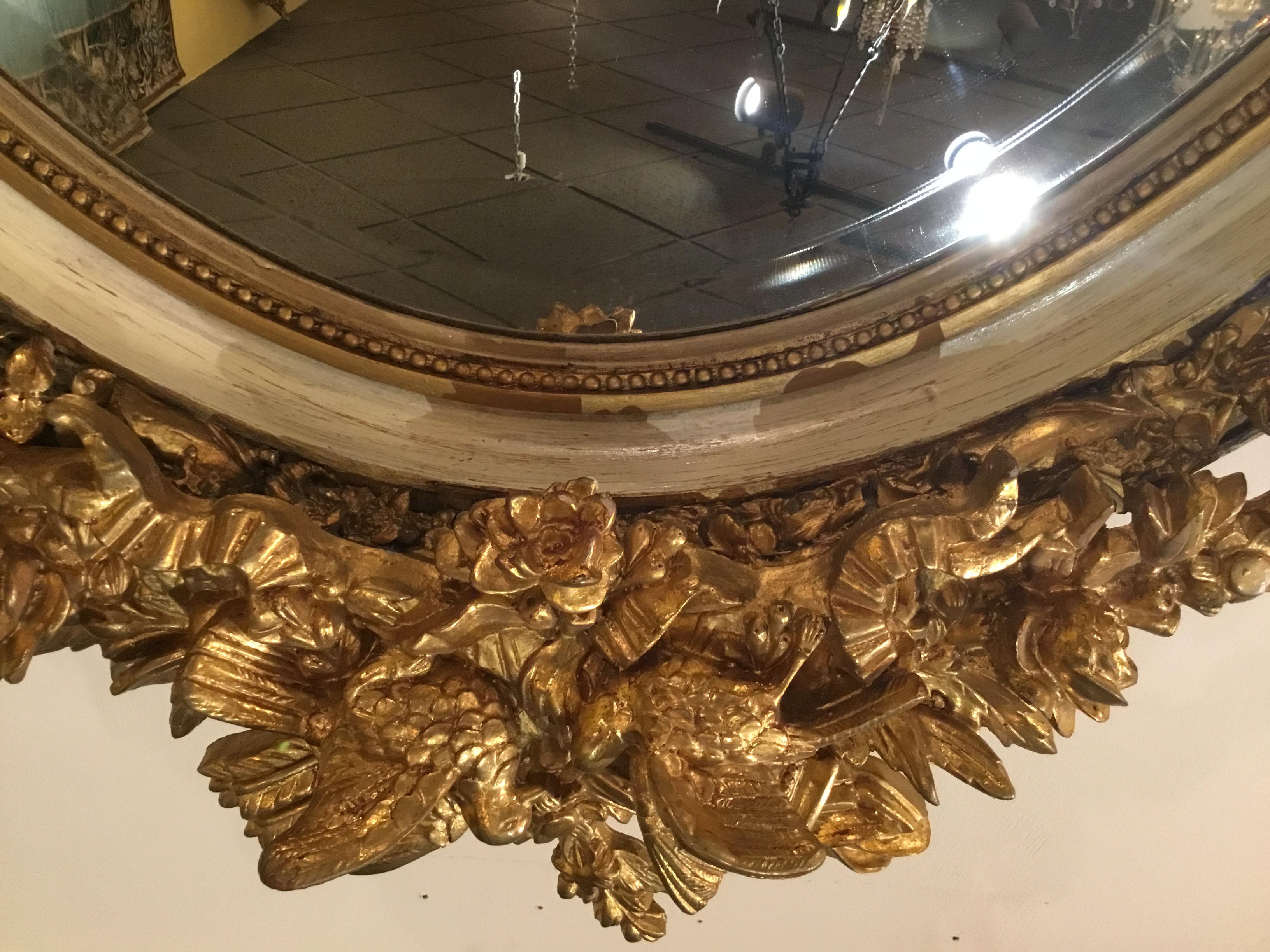 Large pair of oval mirrors with clear and beveled plate. Gilt beading surrounds
The mirror. A cream paint on both the inner edge and the outer edge is
Between a foliate design and the outer edge. A pair of gilt kissing doves
Sits at the crest
