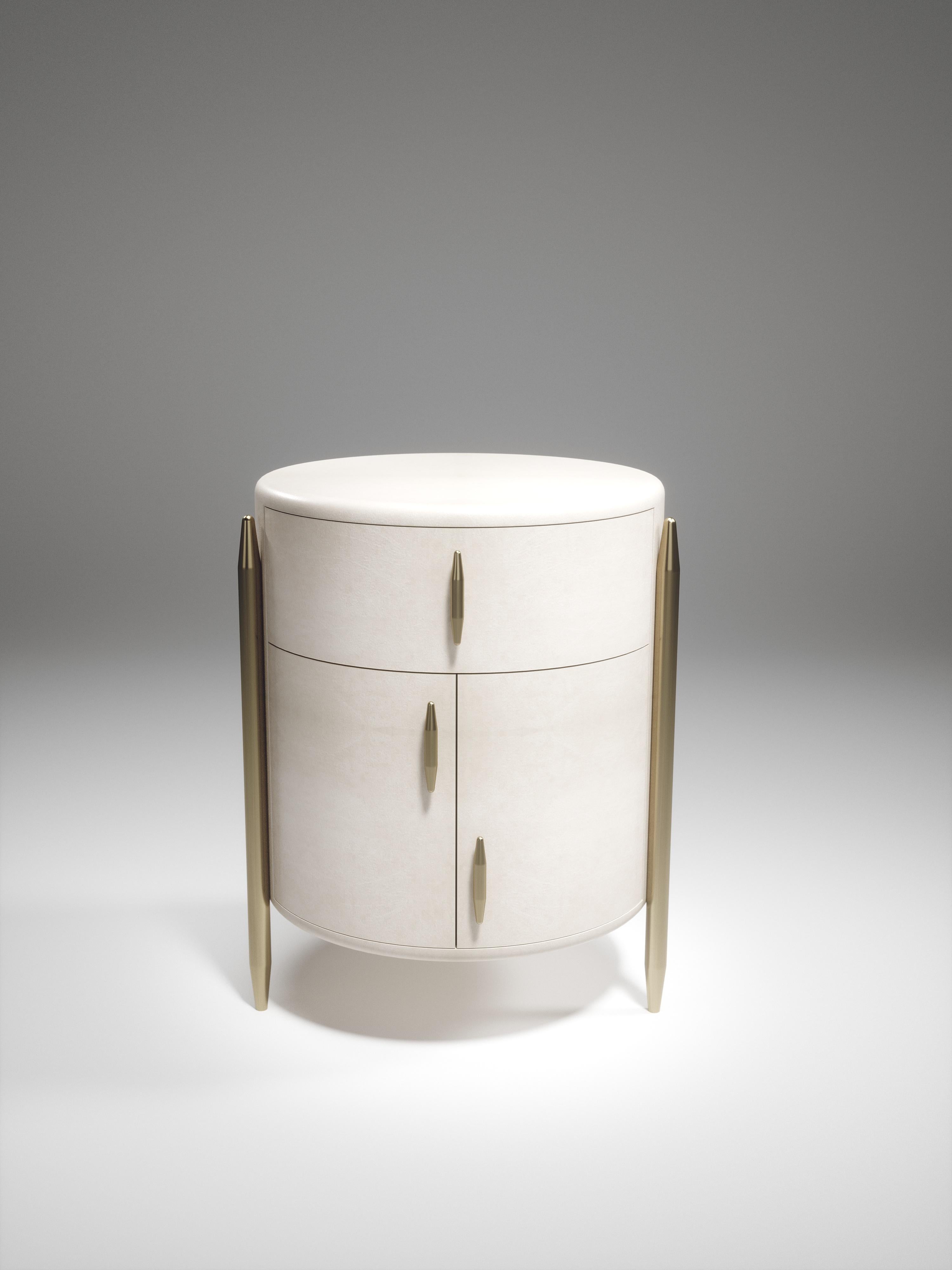 The pair of Dandy round bedside table by Kifu Paris is an elegant and a luxurious home accent, inlaid in cream parchment with bronze-patina brass details. This piece includes 1 drawer total and a cabinet below; the interiors are inlaid in gemelina