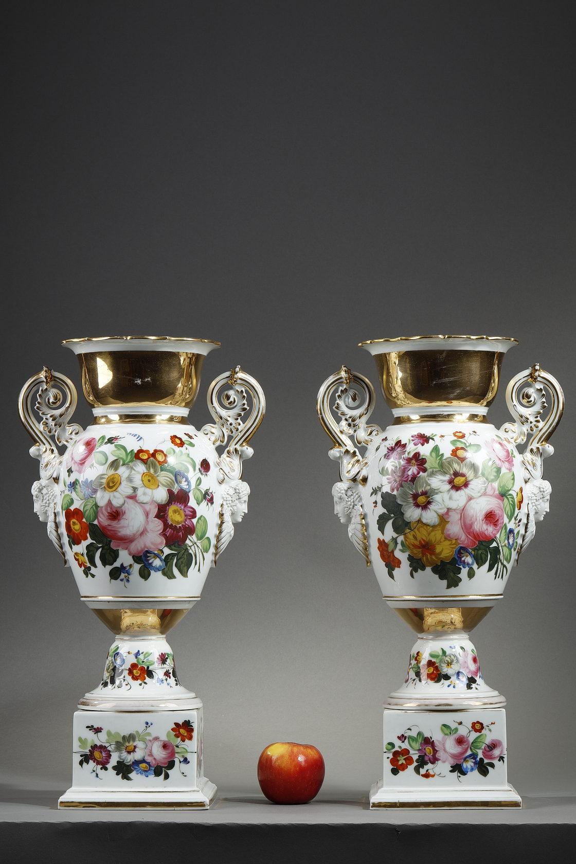 A pair of Paris porcelain baluster vases with polychrome and gold decoration. They have two side handles in volutes decorated with acanthus leaves and ending with feminine faces crowned with grapes and oak leaves. The scalloped edges are underlined
