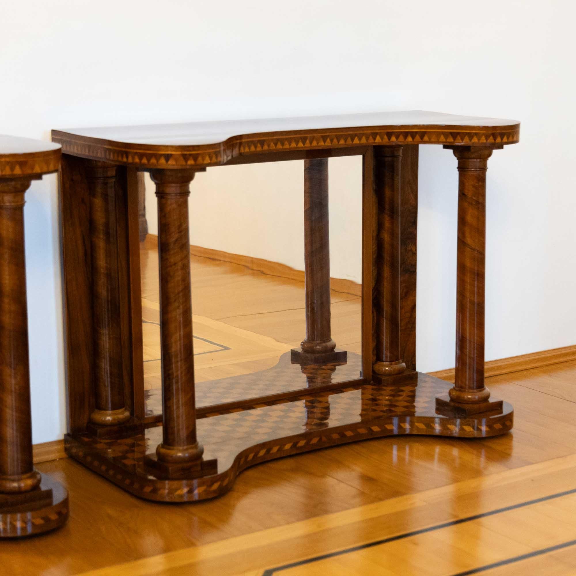 Pair of console tables with mirrored back panels and strong supporting full columns at the front and half columns at the back. The strongly curved top panels correspond with the base and are elegantly inlaid at the edges. The base is also parquetted