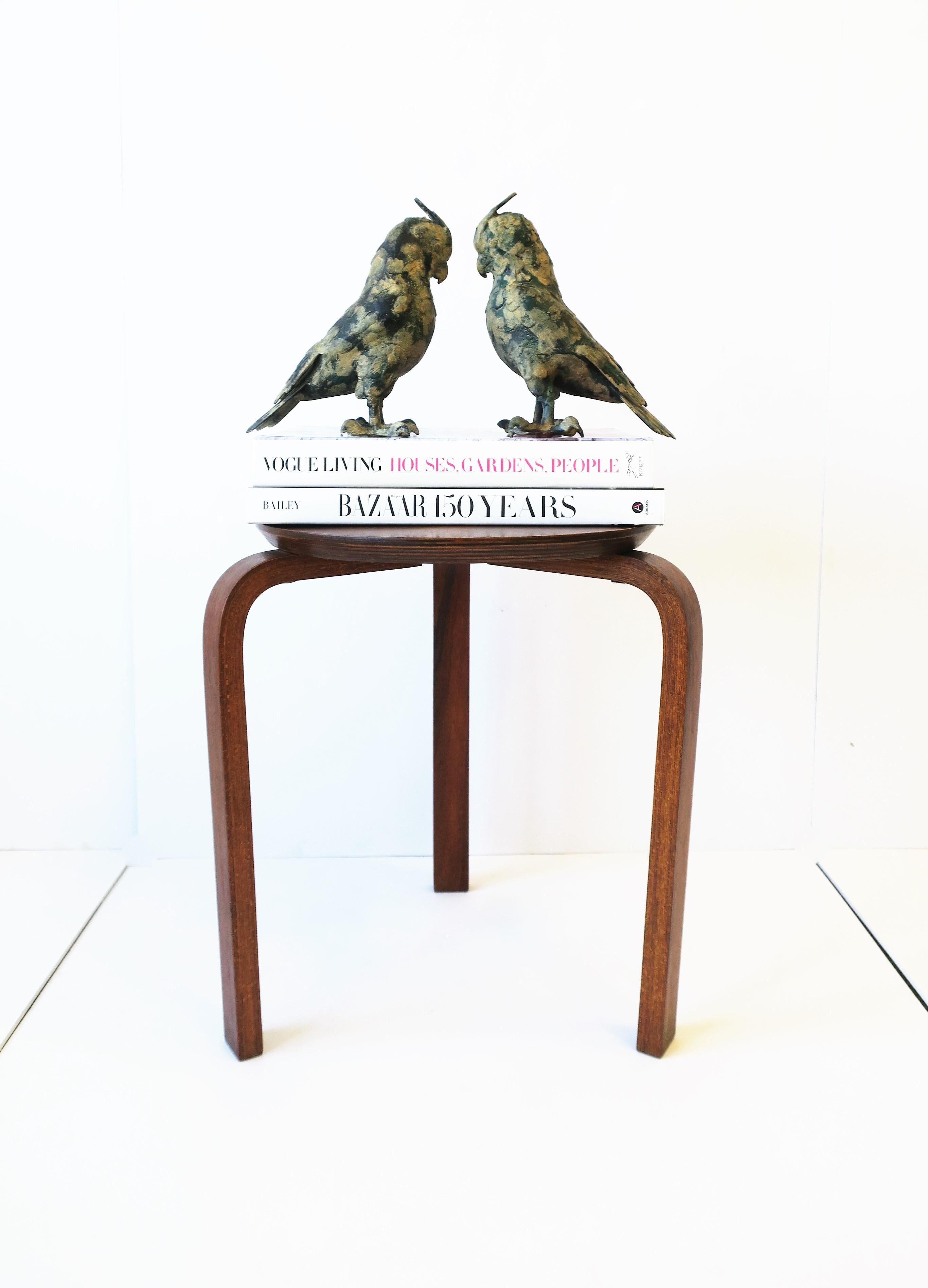 A substantial and striking pair of vintage parrot bird sculptures made of iron and hand painted in black, tan and hunter green hues. Each hold all the true details of a parrot such as their crest (head feathers), feet/claws, bill/beak, and elaborate