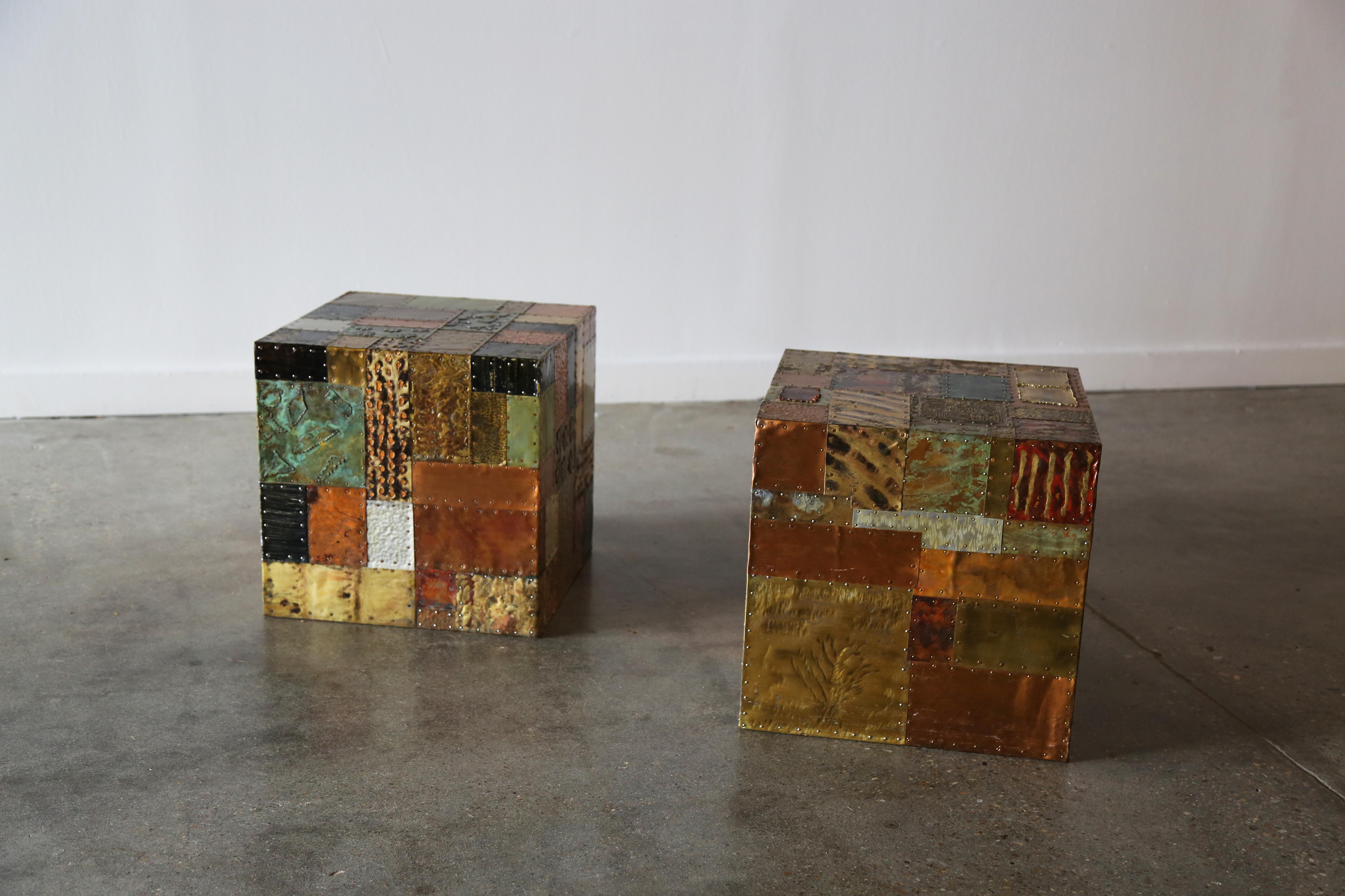 A vintage pair of cube tables made of plywood with mixed metal veneers in a patchwork manner. Great mix of metals from brass, and aluminum to steel, painted in hues of orange, reds, greens, blacks and golds. Relief patterns and bunching provides