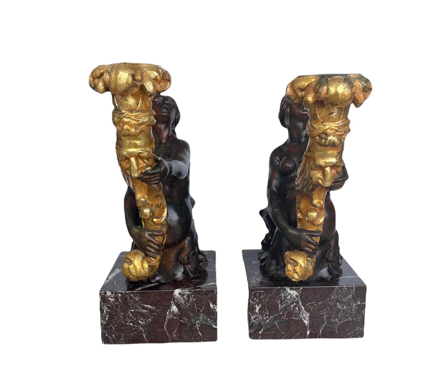 This is a pair of large heavy patinated bronze mermaids sculptures torcheres and/or candelabras. Both depict a half hair styled head and naked trunk kneeled woman with a fish scaly lower body that is holding a gilt bronze torch. Each one of them are