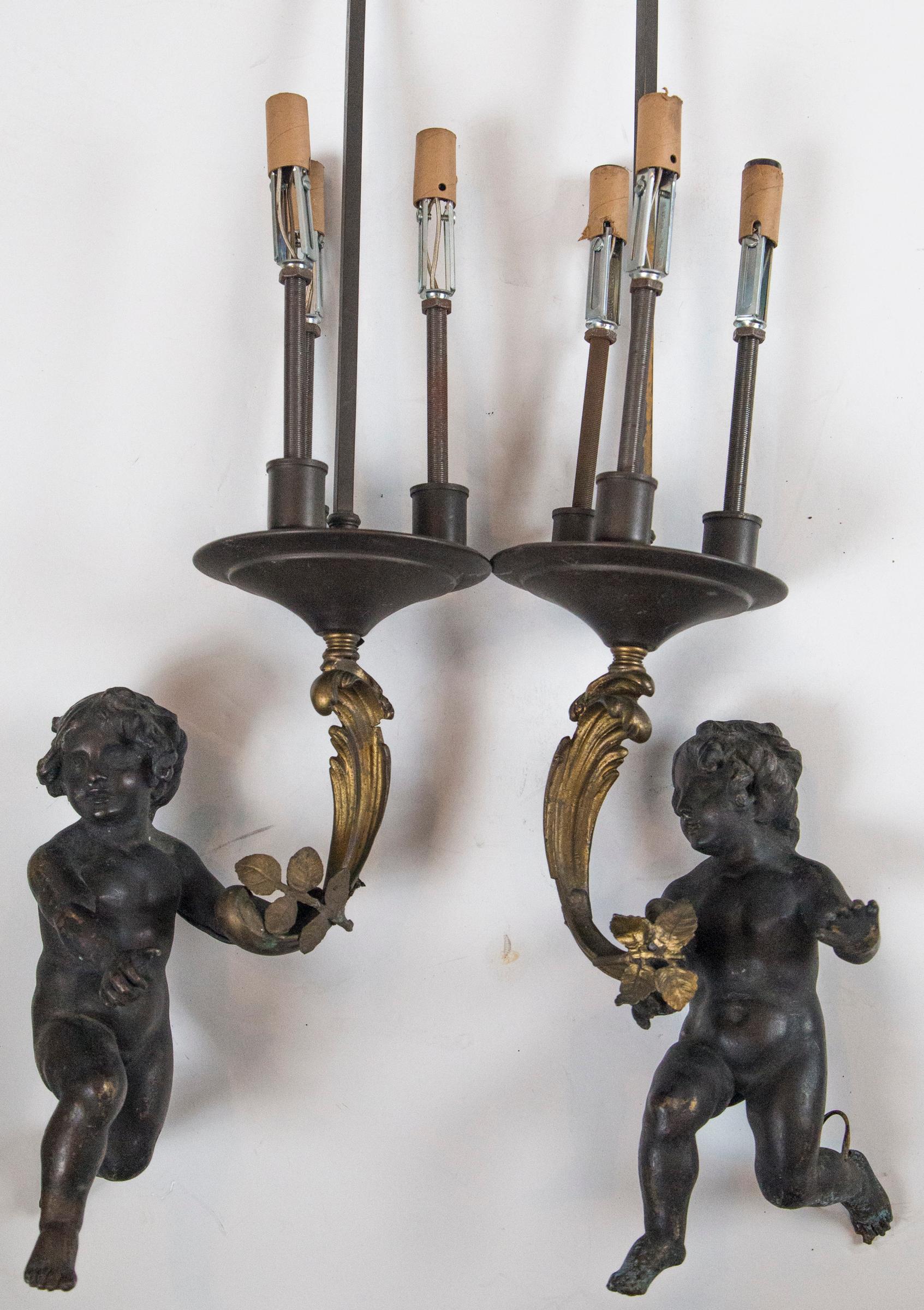 A pair of bronze putti hold a C-scroll of gilt bronze, below a pan disc measuring 6 inches in diameter. There are 3 lamping elements attached to the disc. A bronze rod with final rises above. Offered as is.