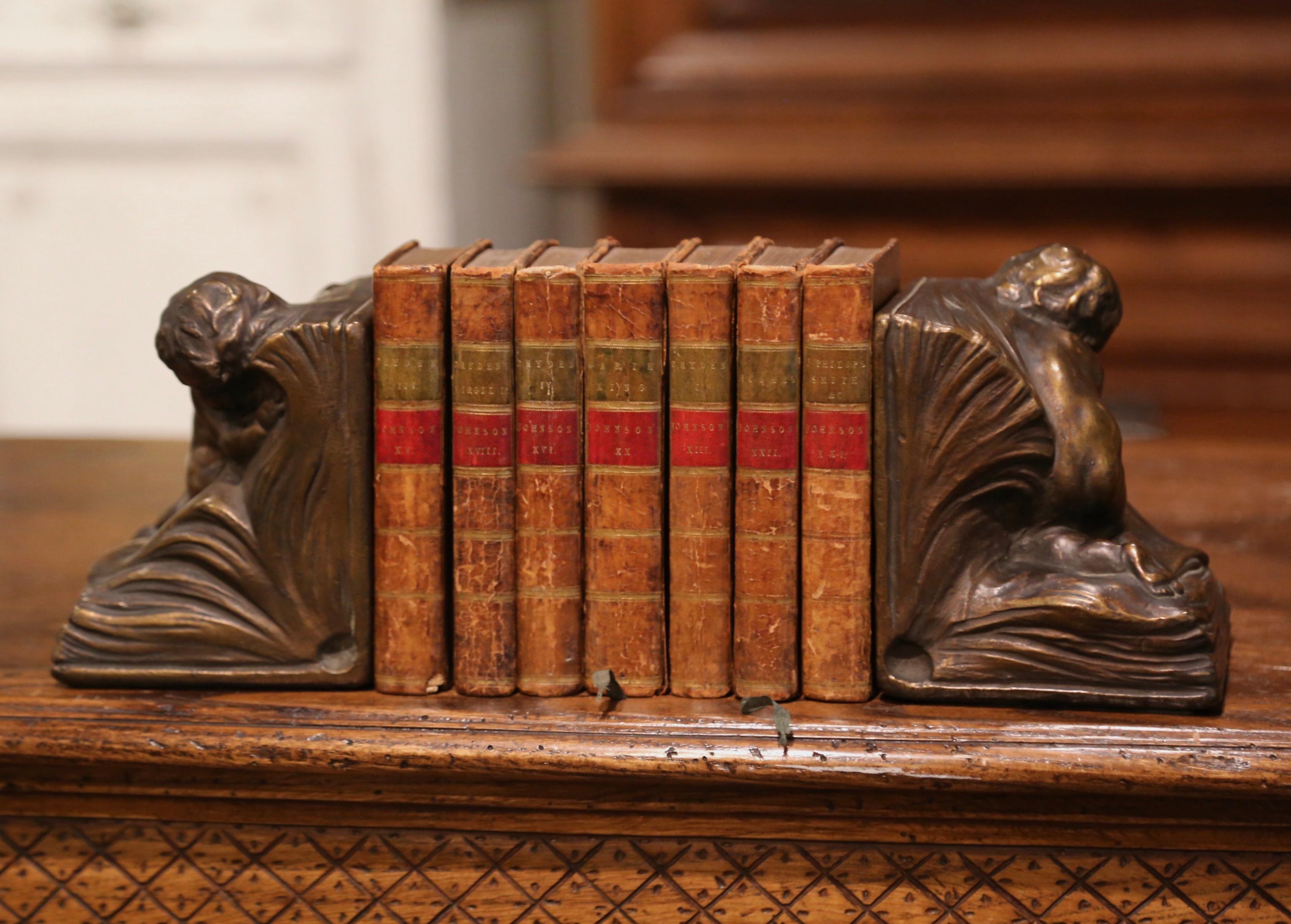 Decorate a study or library with this elegant pair of cheerful angel bookends. Crafted of armor bronze circa 1914, and signed C A Johnson on the back, each antique book stop depicts a cherub sleeping inside an open book. Both decorative bookends are