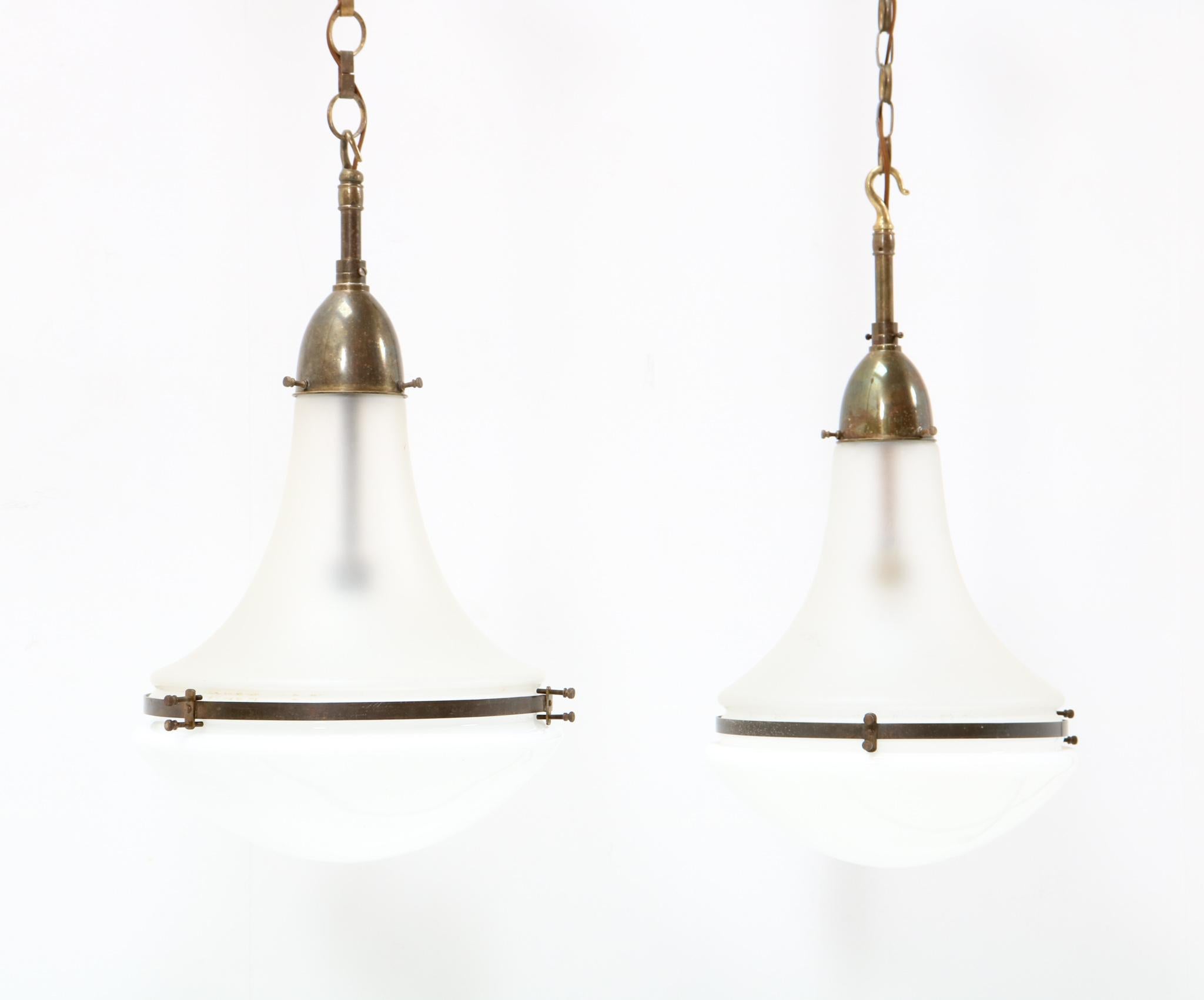 Amazing and rare pair of Art Nouveau Luzette pendant lamps.
Design by Peter Behrens for Siemens.
Striking German design from the 1900s.
Patinated brass with original satinated glass shades on top and original opaline glass shades under.
Both