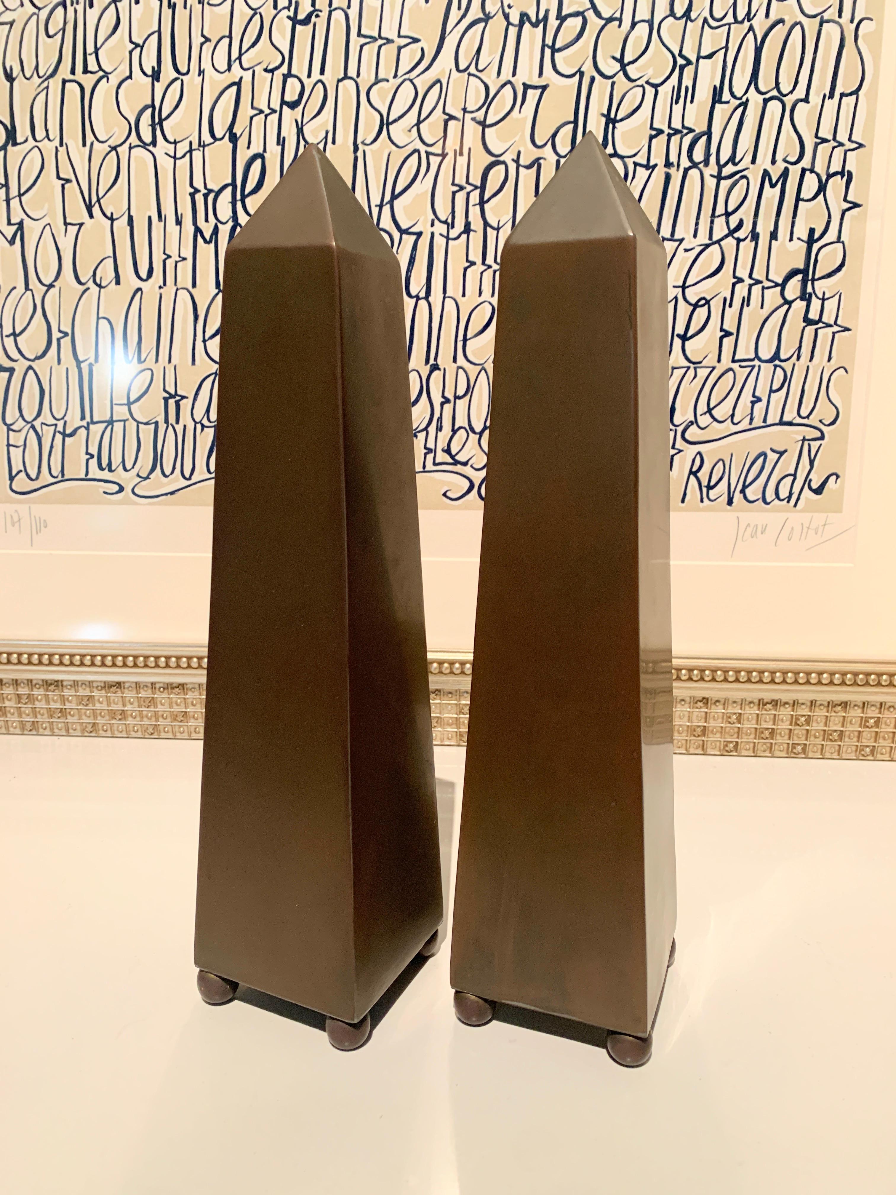 A wonderfully simple and elegant pair of Obelisks. Patinated Brass with spherical feet. The pair would be a nice compliment to any shelf, console table and books, or desk. A lovely and understated pair.