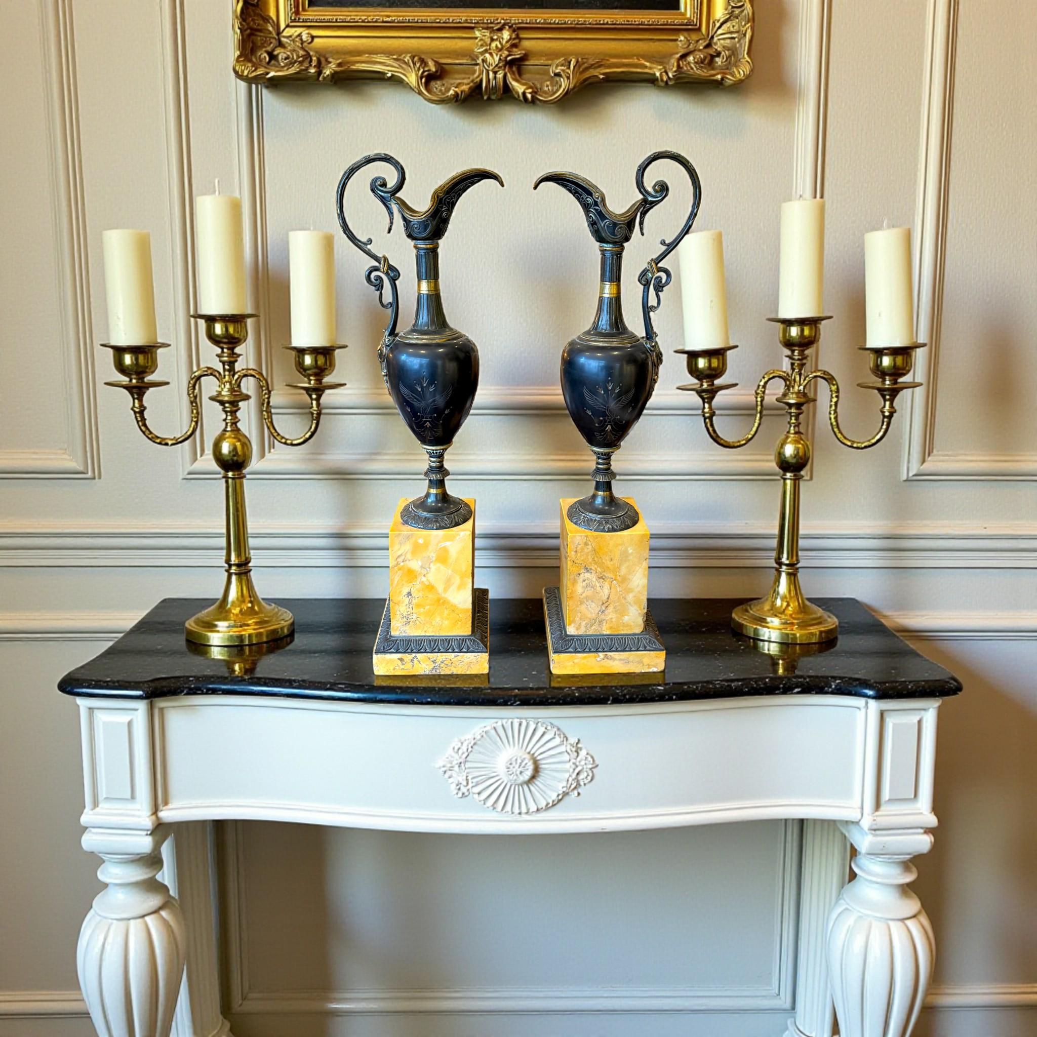 Elegante coppia di grandi feritoie in bronzo patinato scuro, montate su basi in marmo giallo di Siena ornate da un fregio in bronzo patinato finemente dettagliato. Le proporzioni e il contrasto dei materiali conferiscono a questi pezzi una presenza