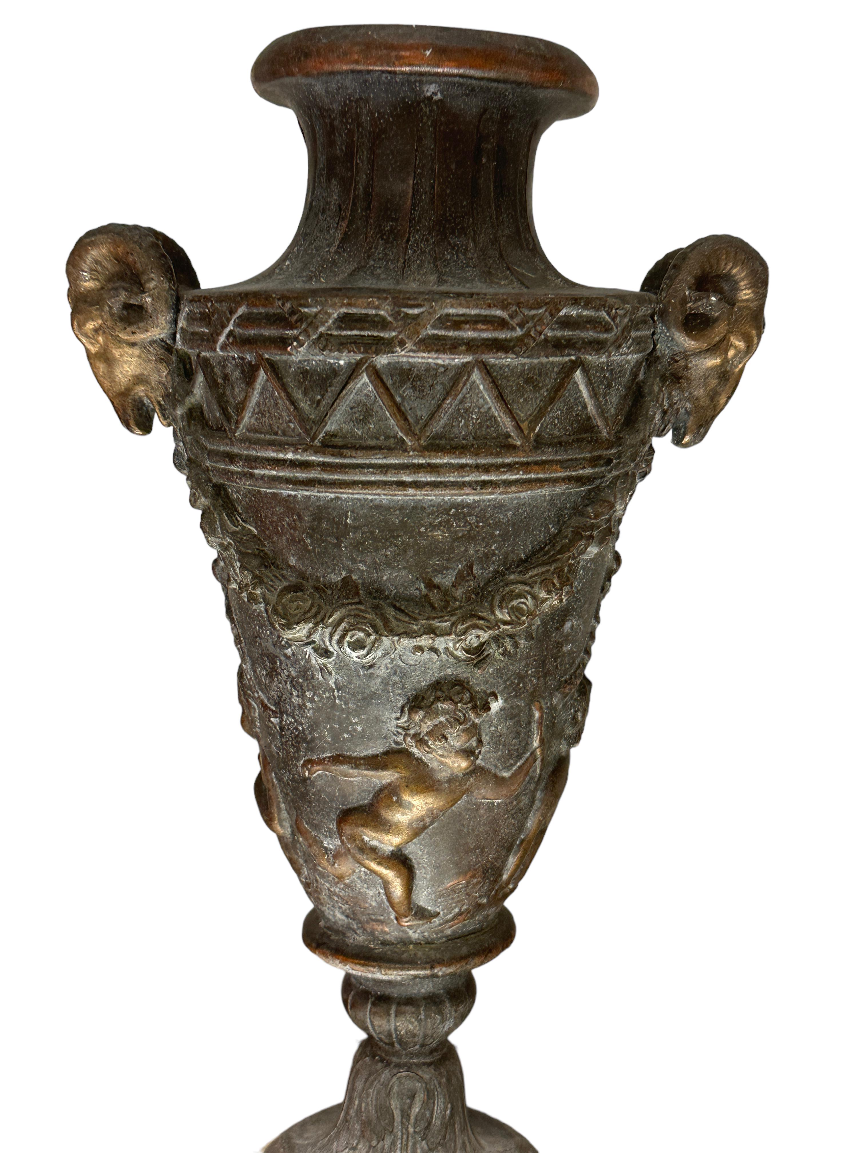 A beautiful pair of patinated bronze Bacchanal vases.
The vases are modeled with masks depicting chimeric ibexes, flanked by laurel garlands, above which are finely carved reliefs of young Cherubs running. Each vase stands on a fluted round marble