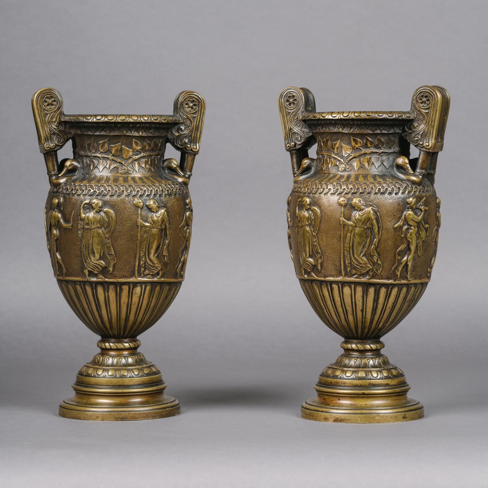 A pair of patinated bronze vases cast after the antique.

Each vase is of krater form with elaborate scrolling volute handles with swan heads and leaf cast necks; the ovoid bodies cast with classical scenes and raised on circular pedestal