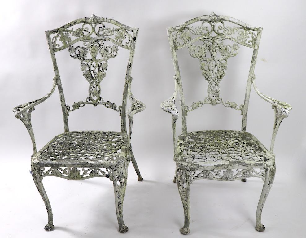Wonderful pair of cast aluminum garden or patio chairs, with exceptionally patinated surface. Classical grape and cable motif armchairs, both are structurally sound and sturdy, one is missing some of the metal frame edge, from seat, as shown.