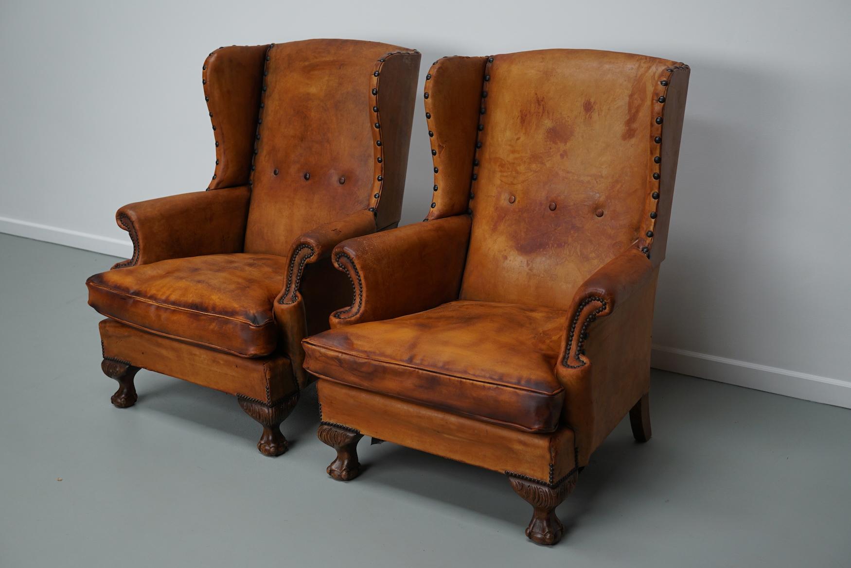Cette paire de fauteuils club en cuir de couleur cognac provient des Pays-Bas. Ils sont recouverts de cuir de couleur cognac et présentent des rivets en métal et des pieds en bois. Ils présentent de nombreux signes d'utilisation et d'âge mais sont