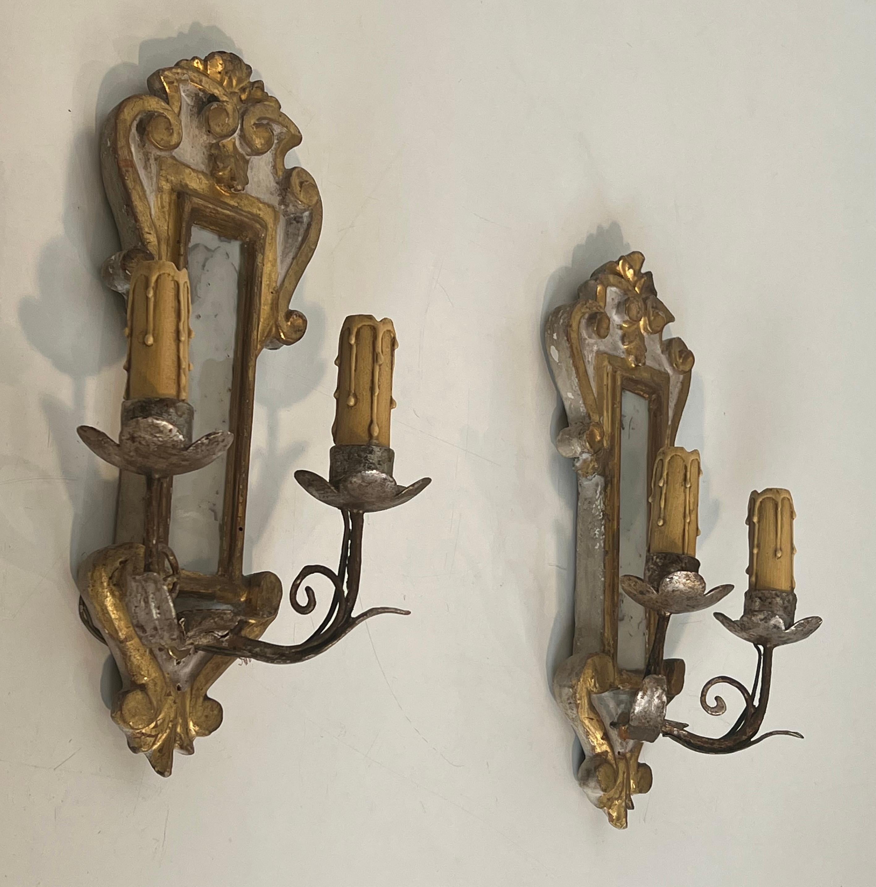 Este bonito y decorativo par de apliques patinados, plateados y dorados es de madera tallada y tiene un espejo en el centro. Se trata de una obra italiana. Alrededor de 1940