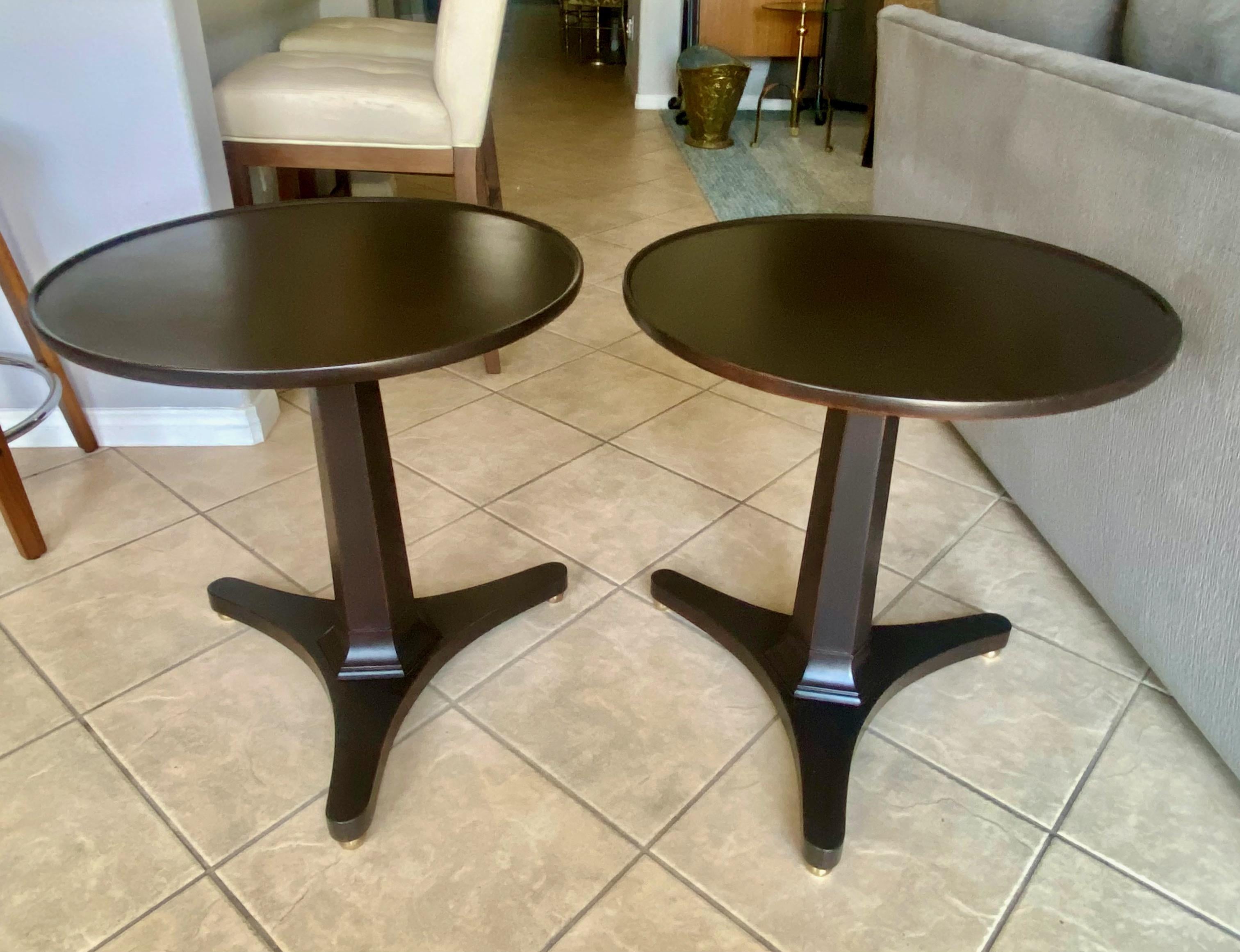 Pair of round top dark walnut/espresso lacquered finish wood side or end tables by Kittinger Furniture Company. Solid hard wood construction tables resting on center post with tripod legs and brass sabot feet. More recently refinished.