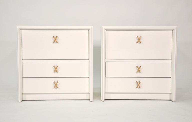 Pair of pristine off-white lacquered and brass end or bedside tables designed by Paul Frankl for Johnson Furniture's Debonair collection, circa 1940. Each occasional table or small chest features a fall front and two drawers fitted with signature