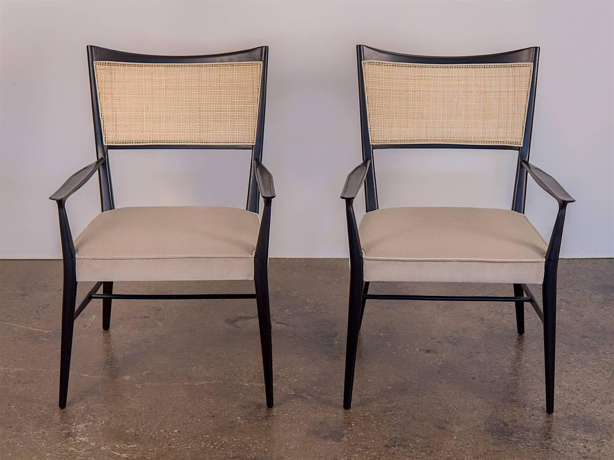 Refined pair of 1950s Paul McCobb Irwin occasional chairs. This pair has been carefully restored with an ebonized finish, and newly upholstered in a plush Romo velvet. Newly woven cane back compliments the neutral cushions, held together by the
